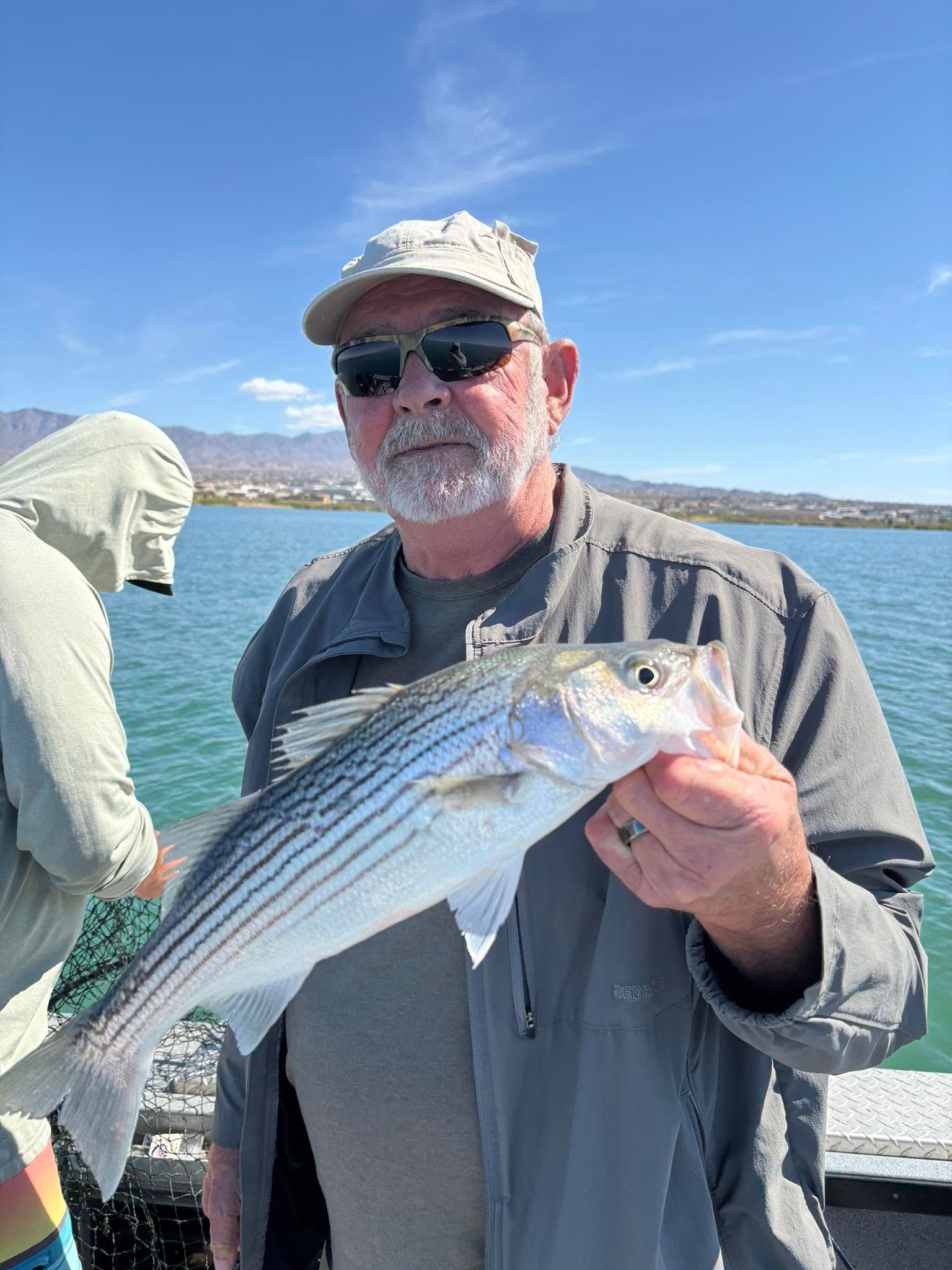 Angler holding freshly caught striped bass on fishing boat with water and mountains in background