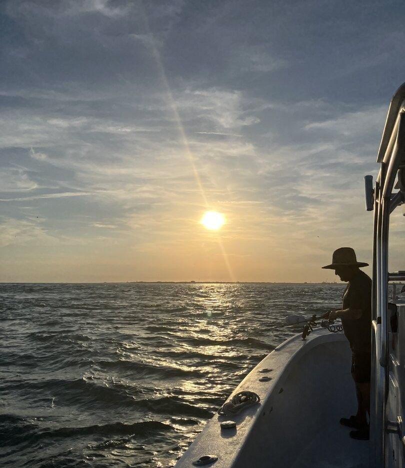 Fishing from boat deck at sunset with golden light reflecting on ocean water