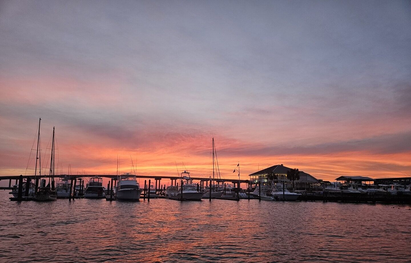 Marina dock with various boats moored at sunset with colorful sky reflecting on water