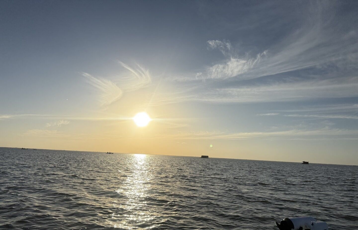 Sun setting over ocean water with boats visible in distance