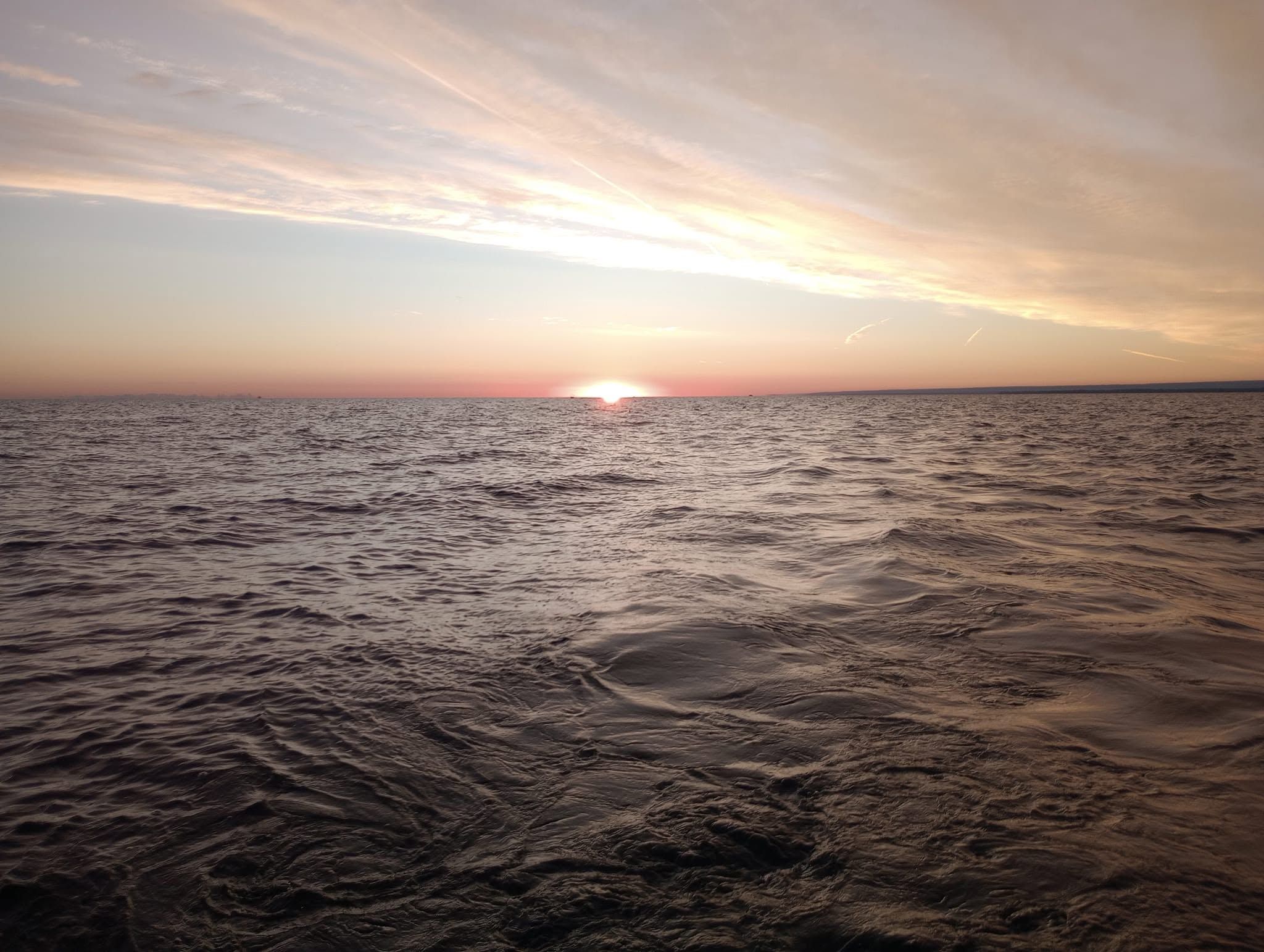 Sunset over calm ocean waters with gentle waves and cloudy sky