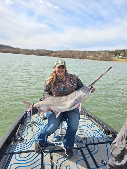 Angler holding large fish on boat deck with lake and hills in background