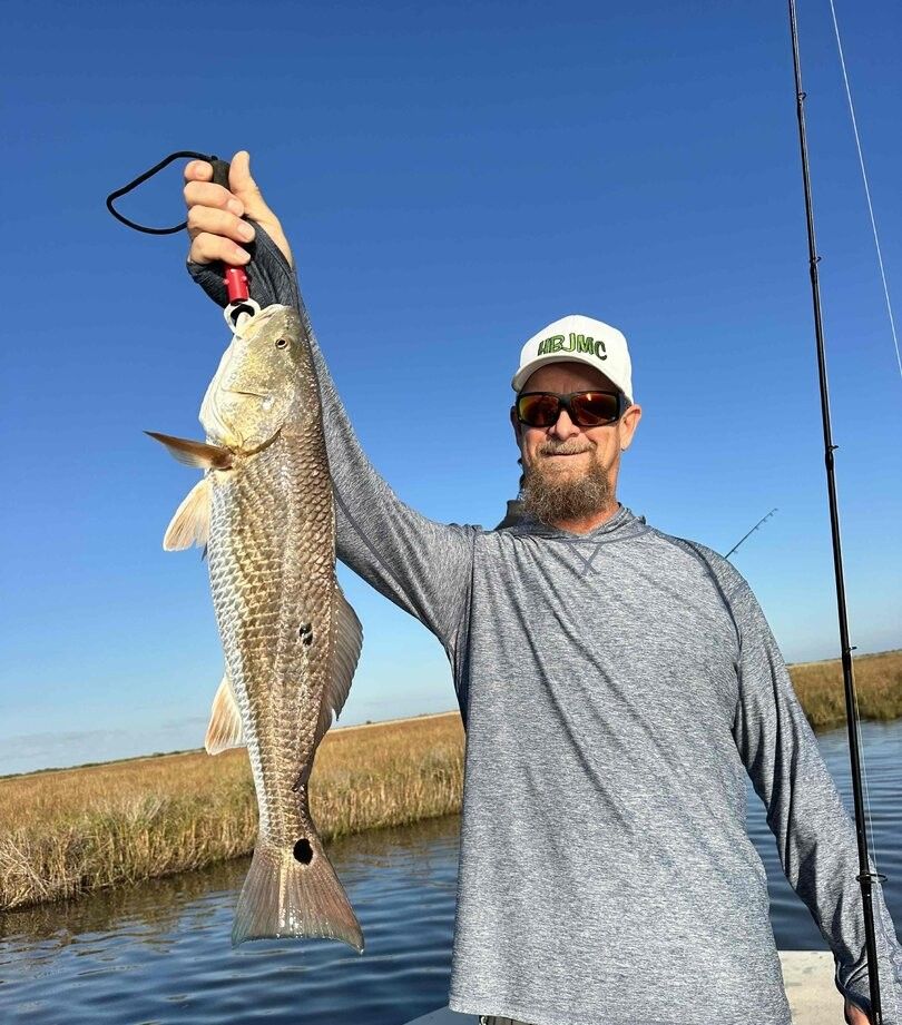 Angler holding large redfish catch outdoors with fishing rod and marsh waterway in background