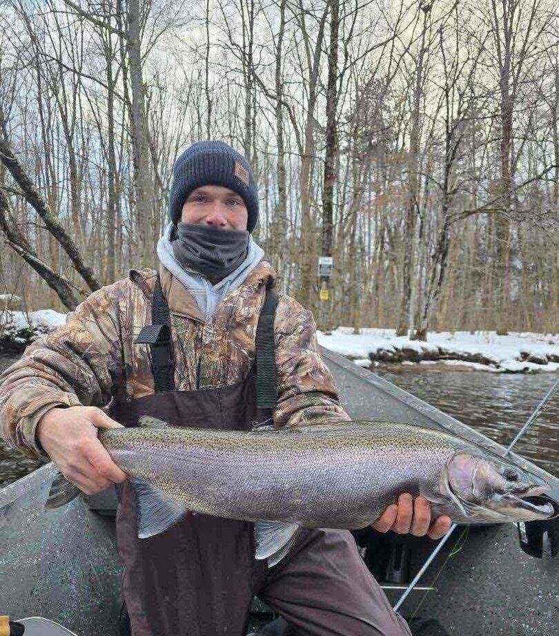 Angler holding large Coho Salmon in winter fishing setting with snow and bare trees