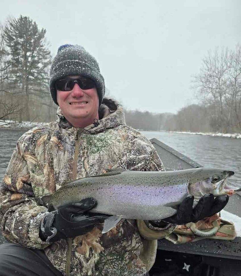 Rainbow trout caught during winter fishing trip with snowy riverbank and bare trees in background
