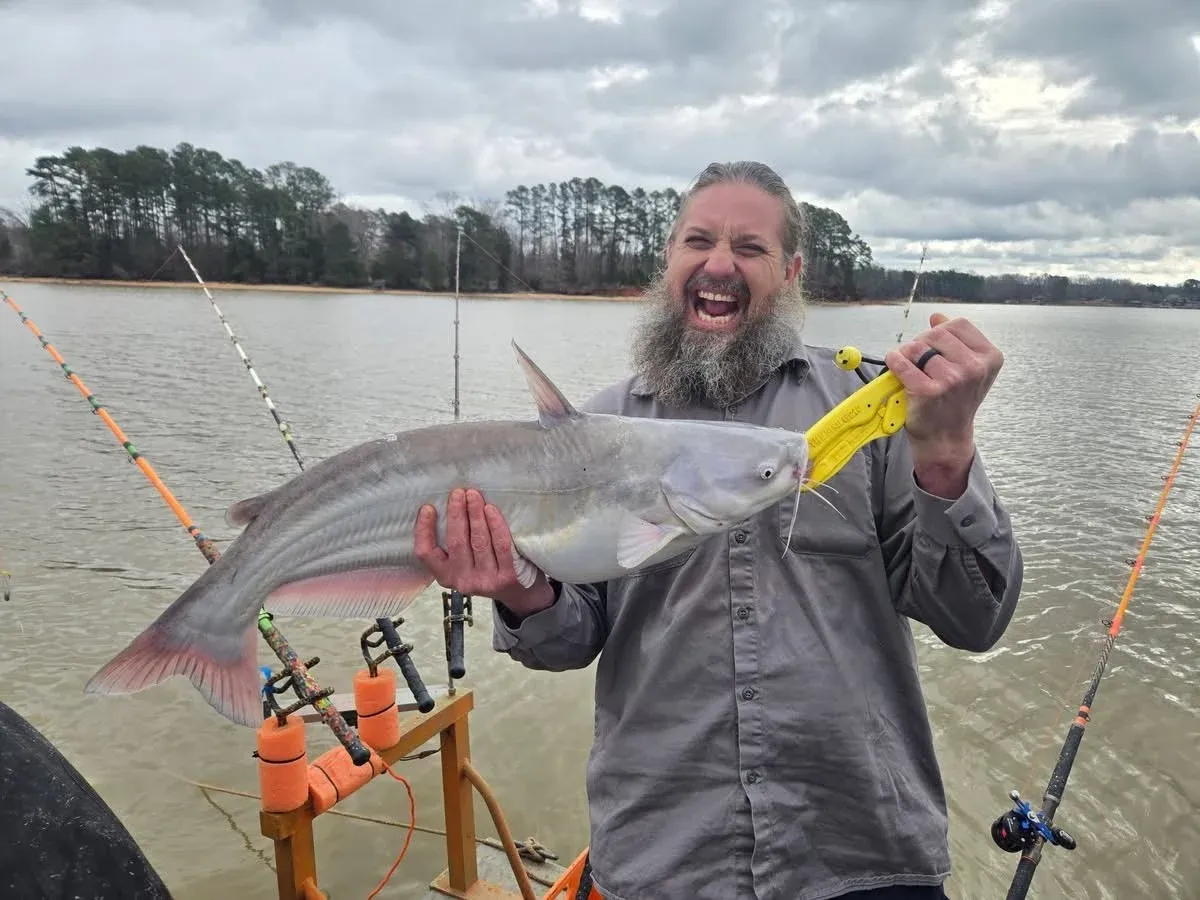 Angler holding large blue catfish on fishing boat with multiple rods