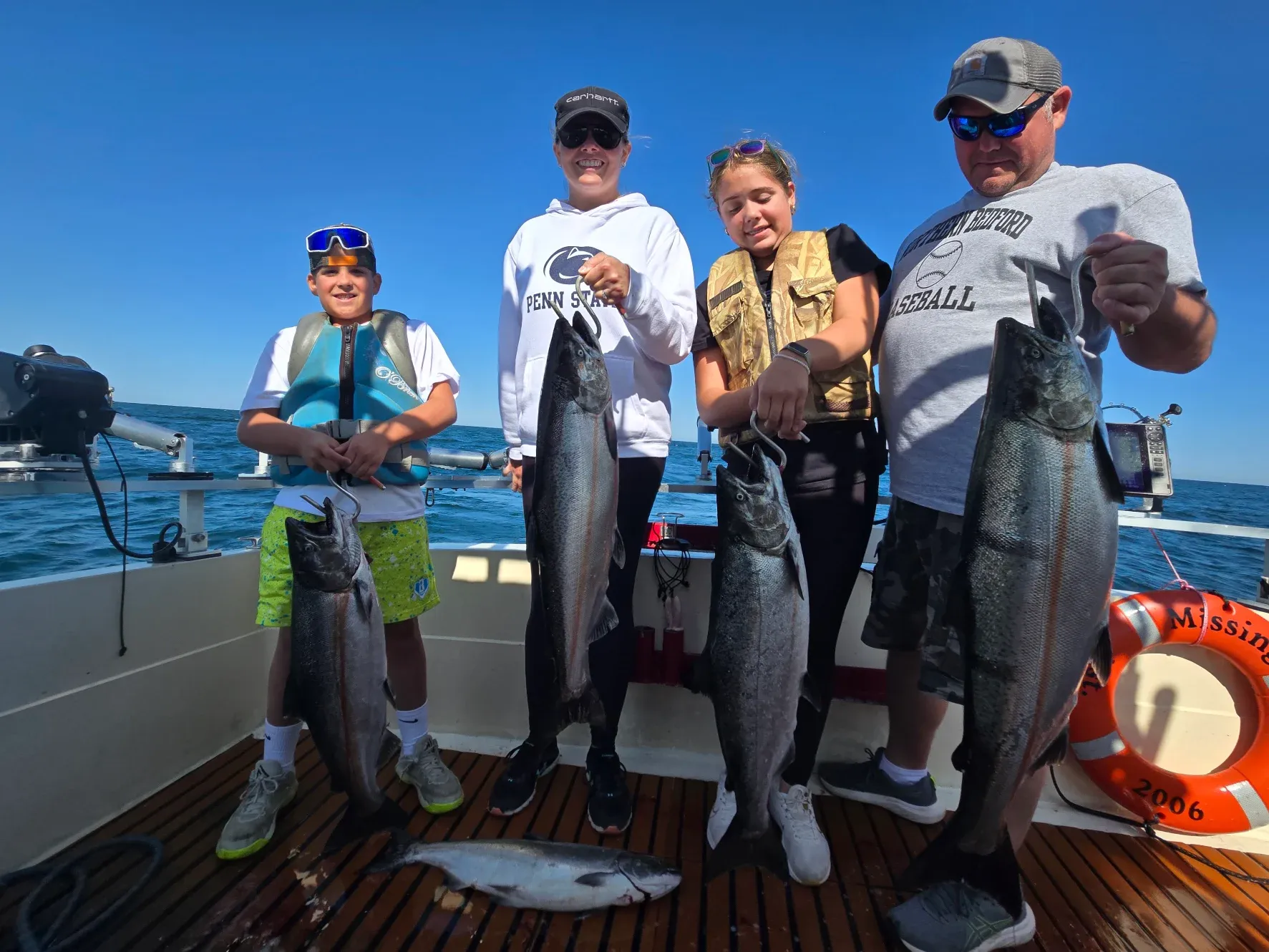 Four people on fishing boat displaying caught Chinook salmon on deck over ocean water