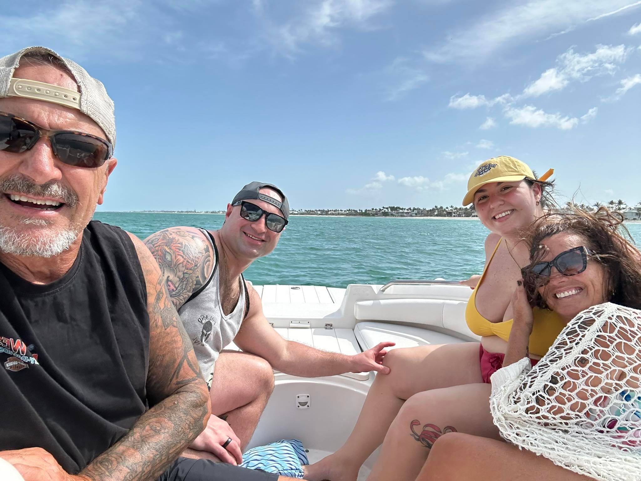 Group enjoying a sunny day on a boat with clear turquoise waters and coastal scenery in the background