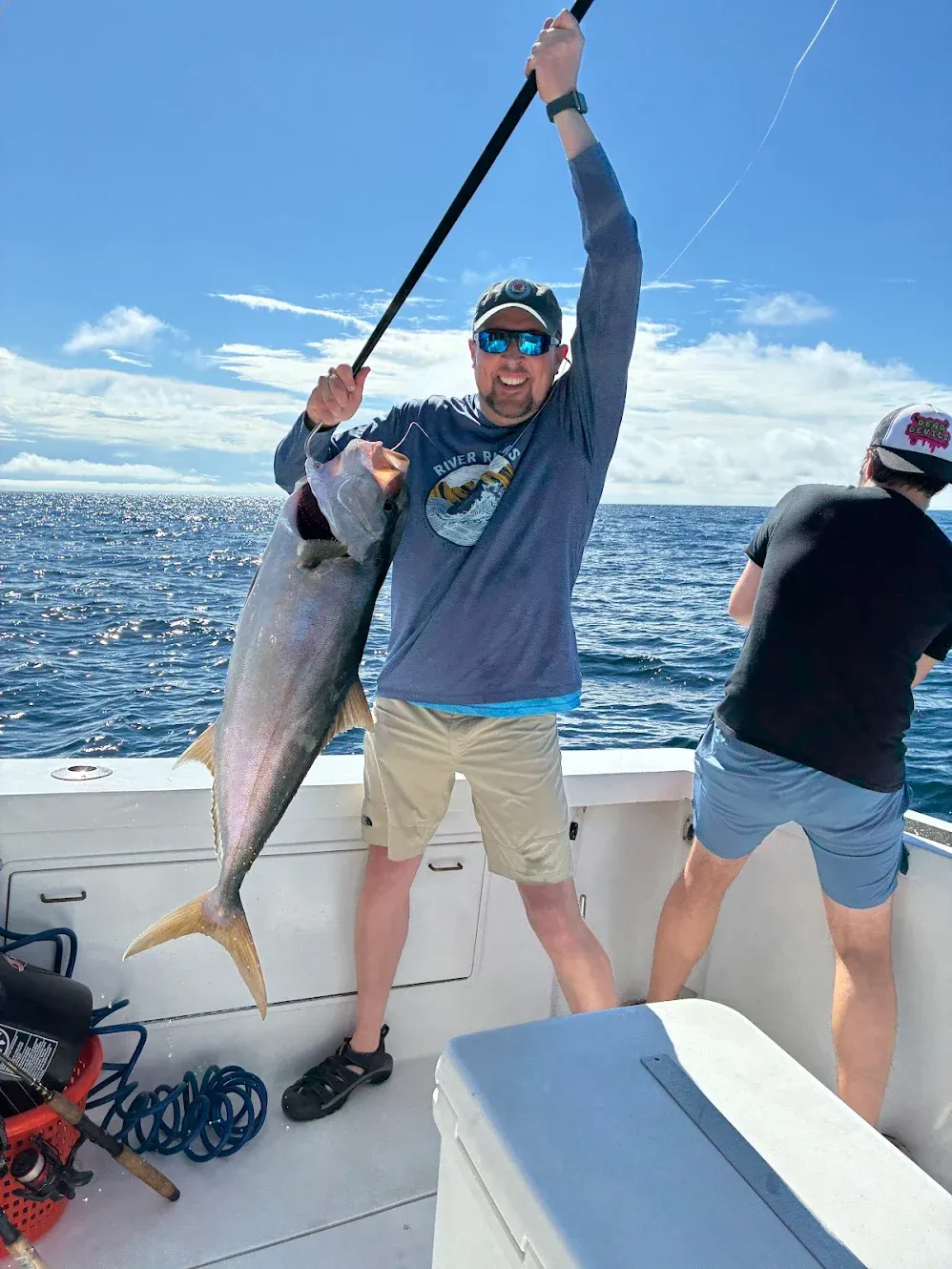Angler holding caught Greater Amberjack fish on fishing boat deck over ocean waters