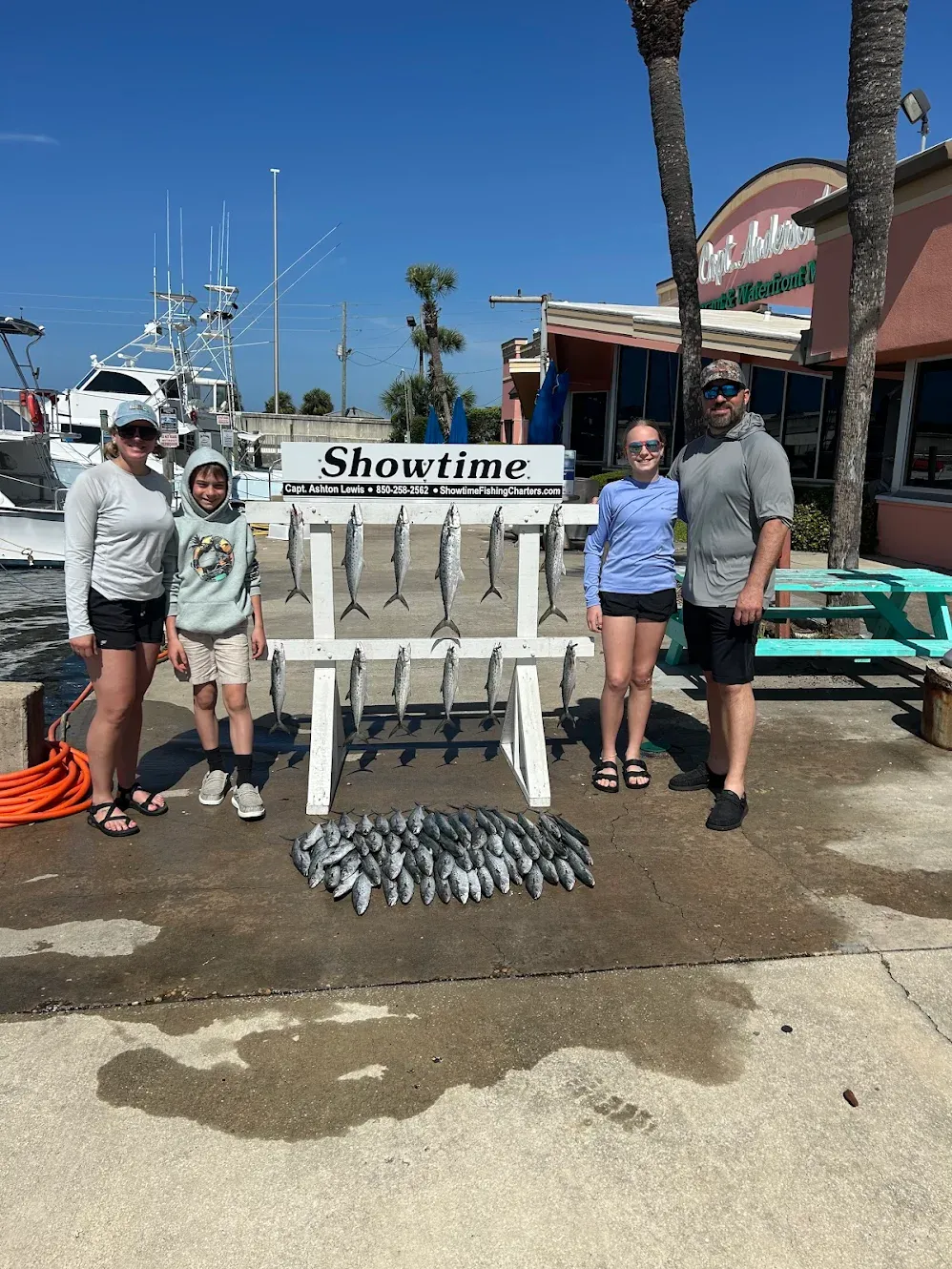 Successful King Mackerel fishing charter displaying large catch on dock with charter boat in background