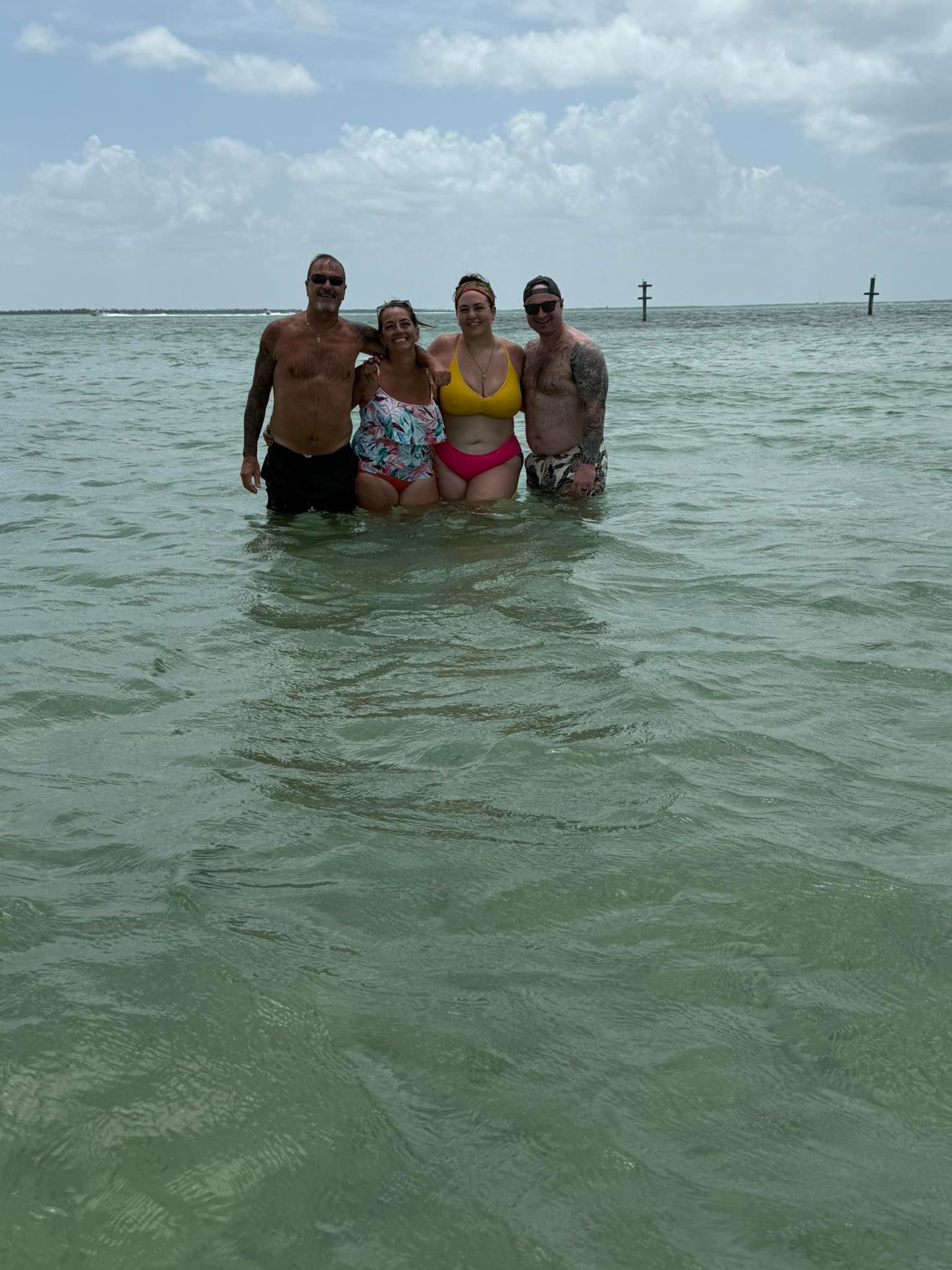Four people standing together in shallow ocean water enjoying a beach day