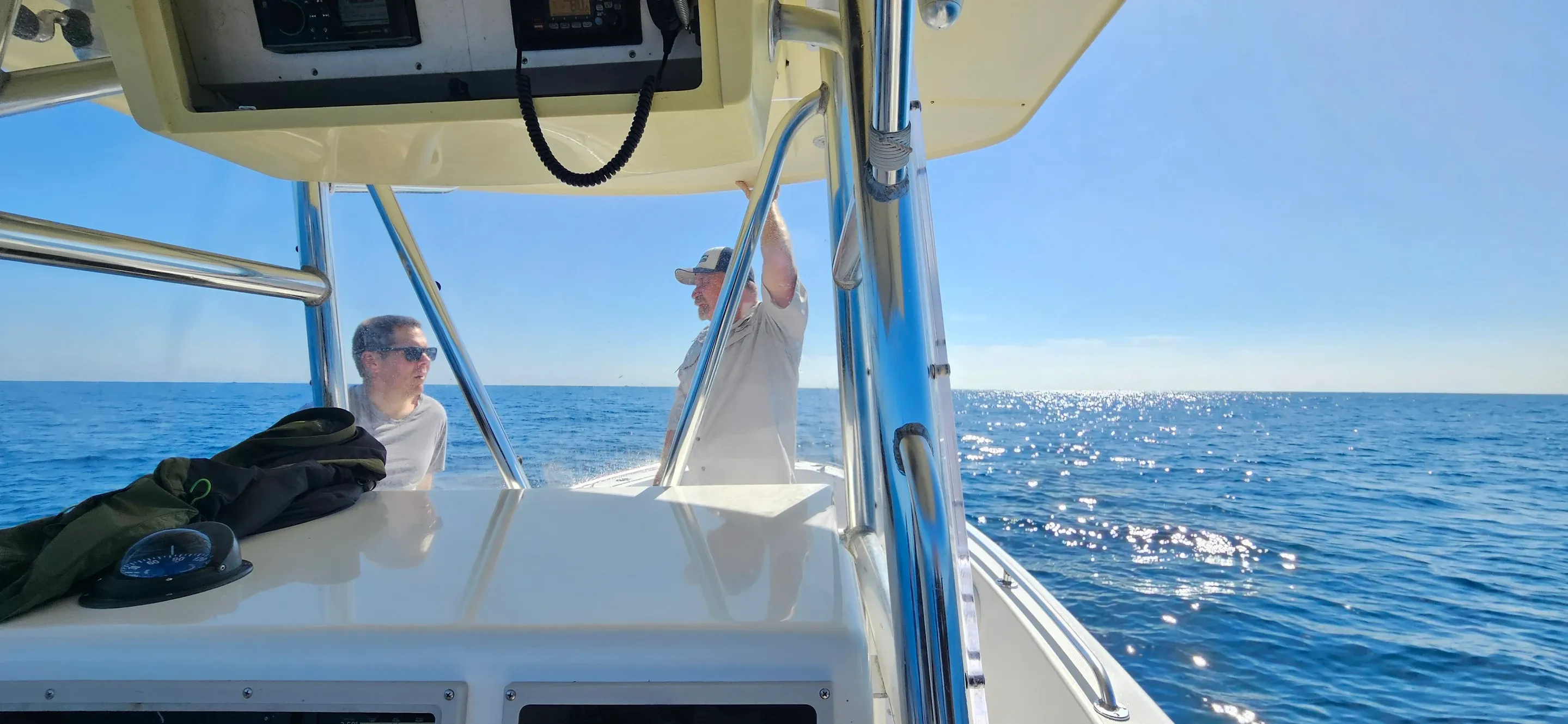 Fishing boat on open ocean water with clear blue sky and sunlight reflecting on water surface