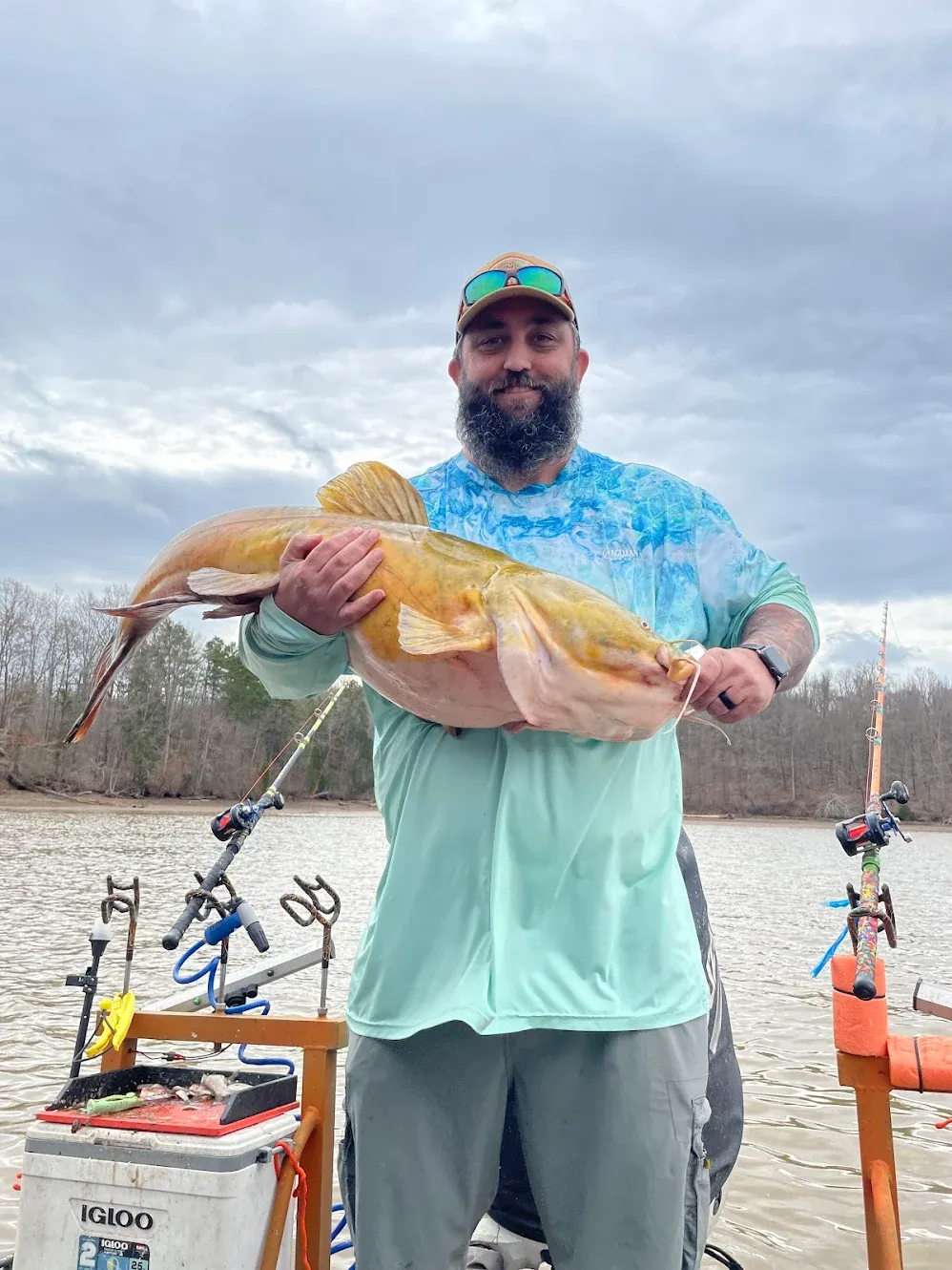 Angler holding large catfish on fishing boat with rods and tackle equipment