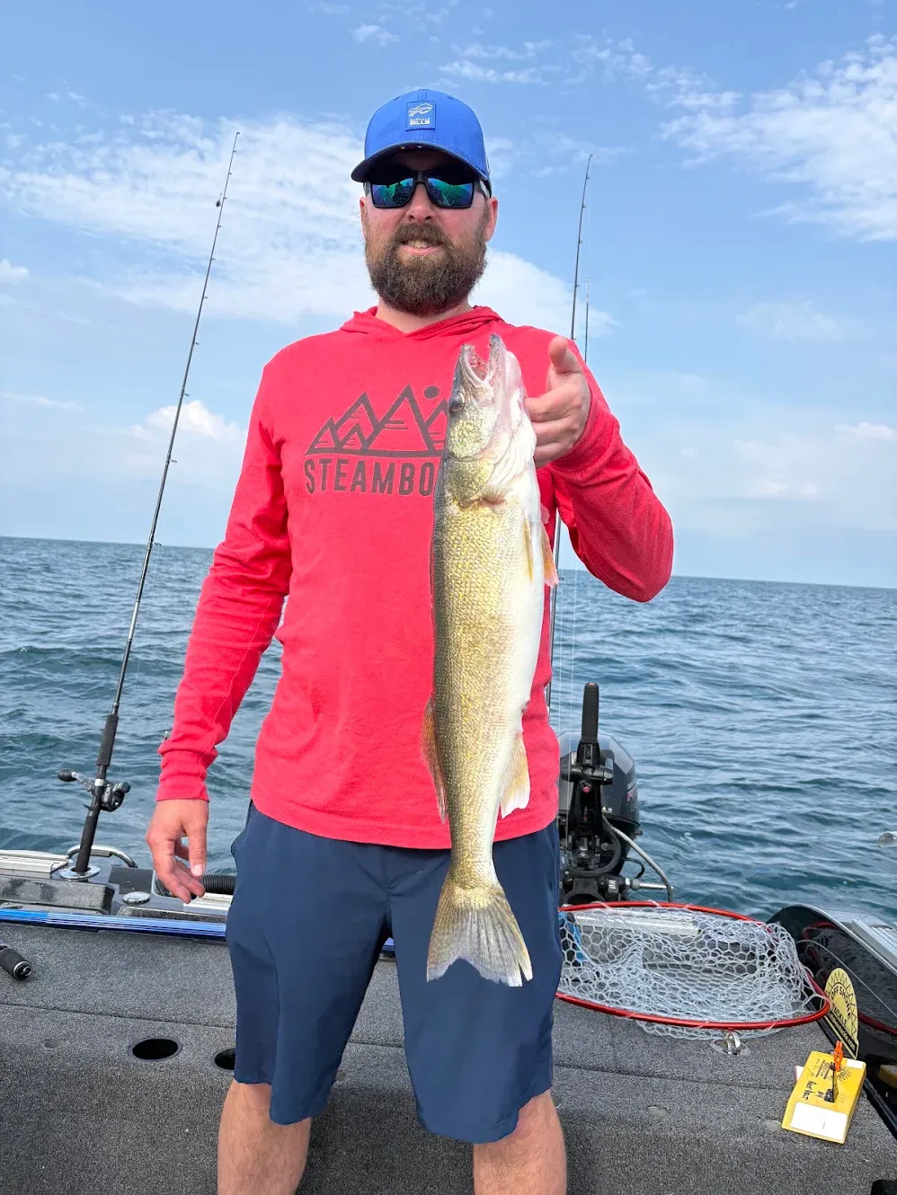Angler holding large walleye fish on boat deck with fishing rods and net visible