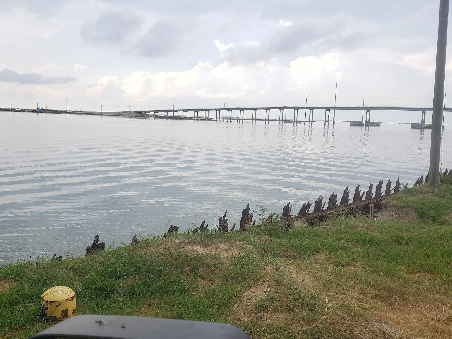 Wooden dock extending over calm water with grassy shoreline and old wooden posts