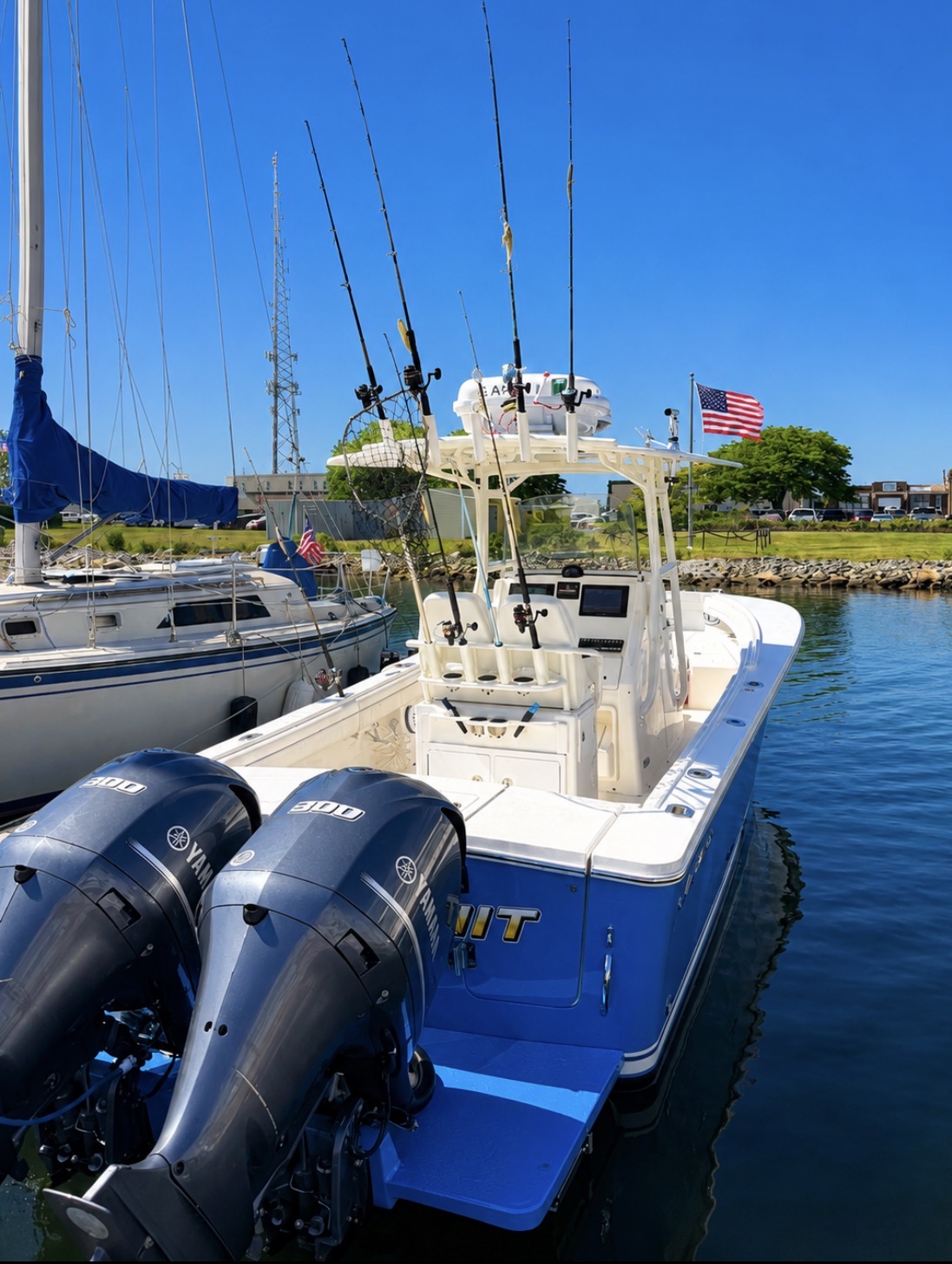 Blue and white fishing boat with twin outboard motors docked at New Bedford MA marina with fishing rods mounted on tower