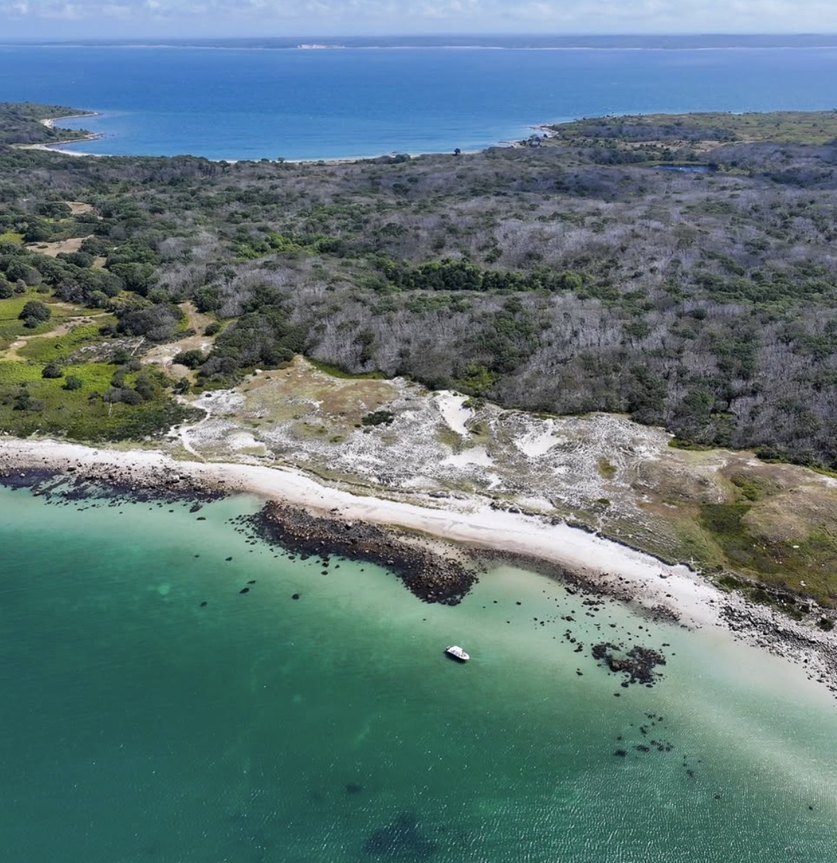 Aerial view of turquoise waters and white sandy beach with small boat anchored in protected cove near New Bedford MA