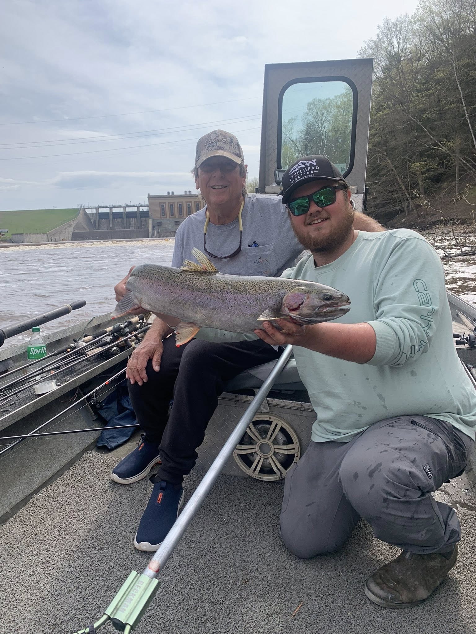 Two anglers displaying a large rainbow trout catch on fishing boat in Brethren MI