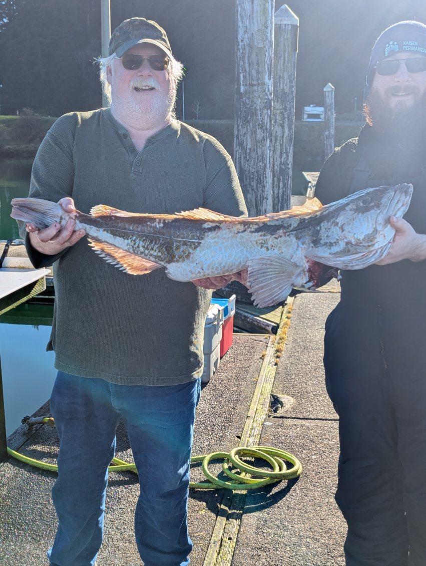 Two anglers proudly displaying a large lingcod catch at a dock in Roseburg OR