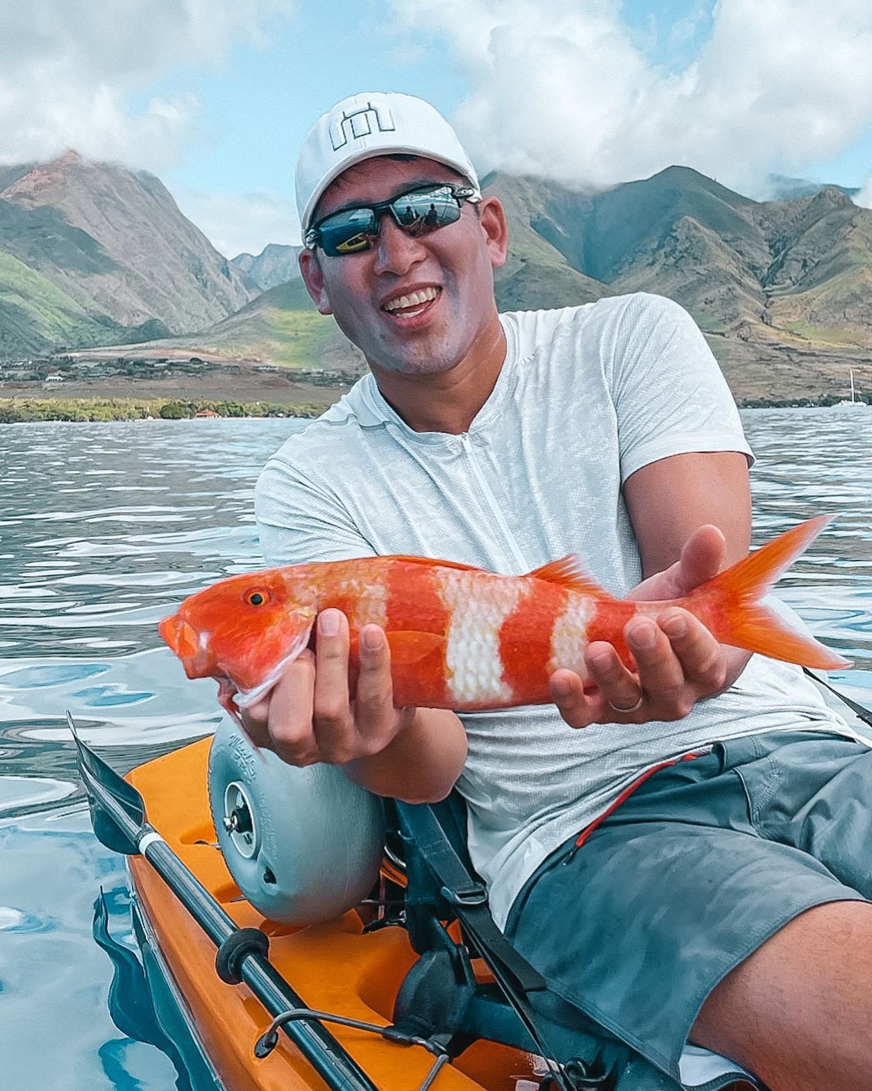 Freshly caught red fish displayed in hands on kayak in Lahaina Hawaii waters with mountains in background