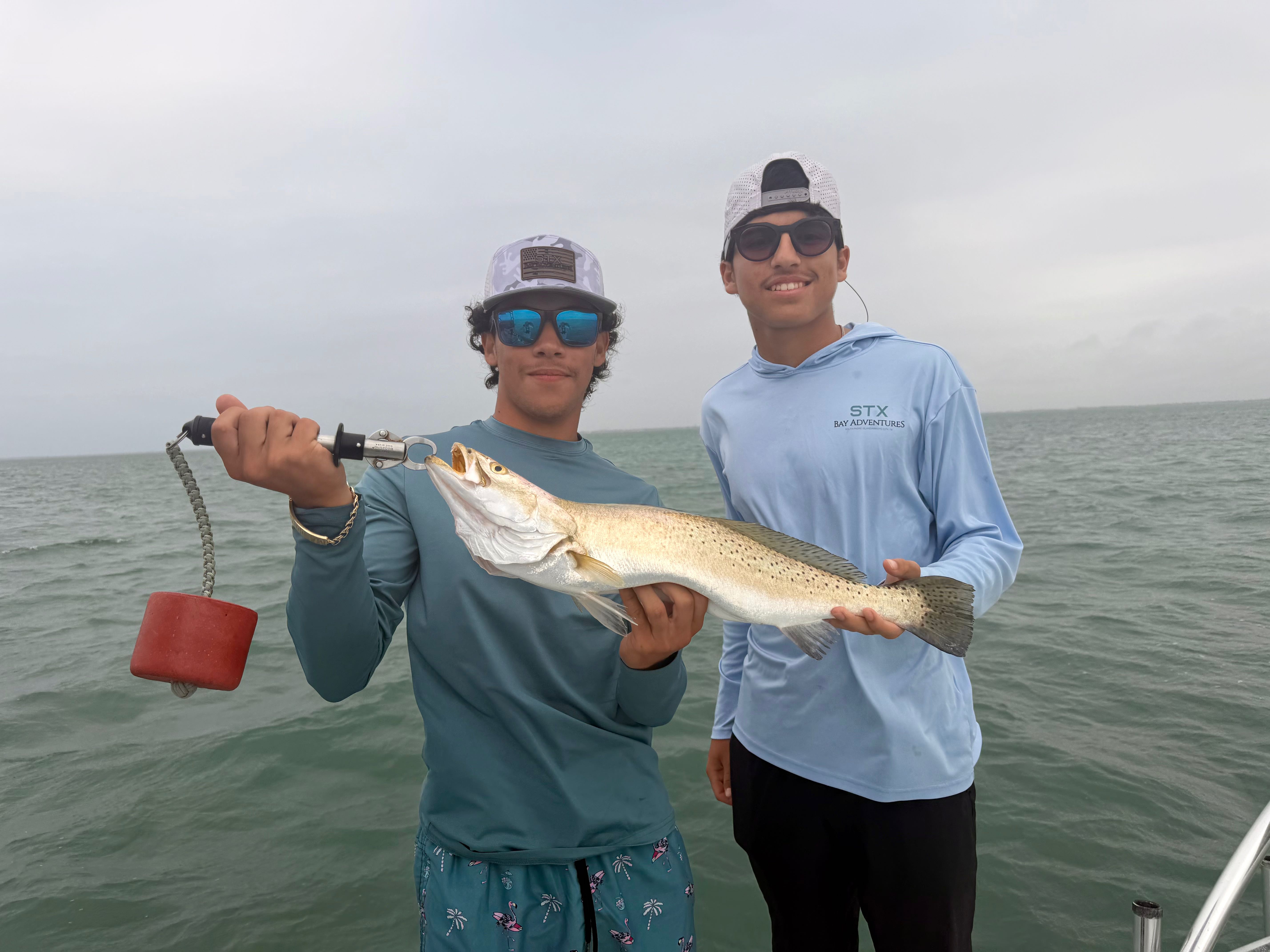 Two anglers displaying a caught speckled trout on fishing boat in Brownsville TX waters