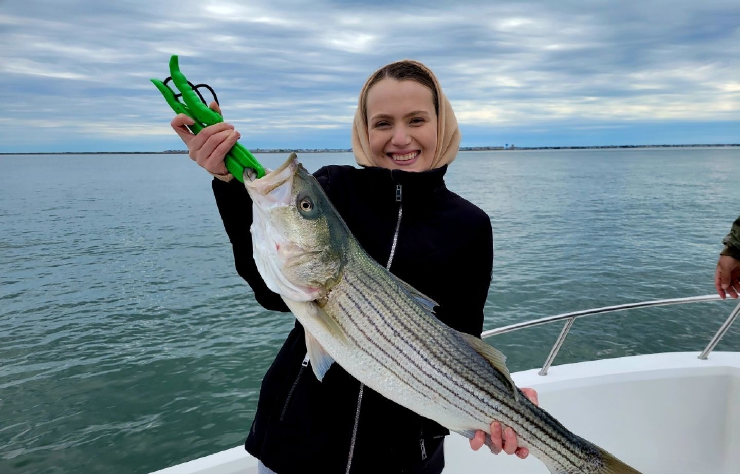 Striped bass catch held with green fish grip tool on boat in Atlantic City NJ waters