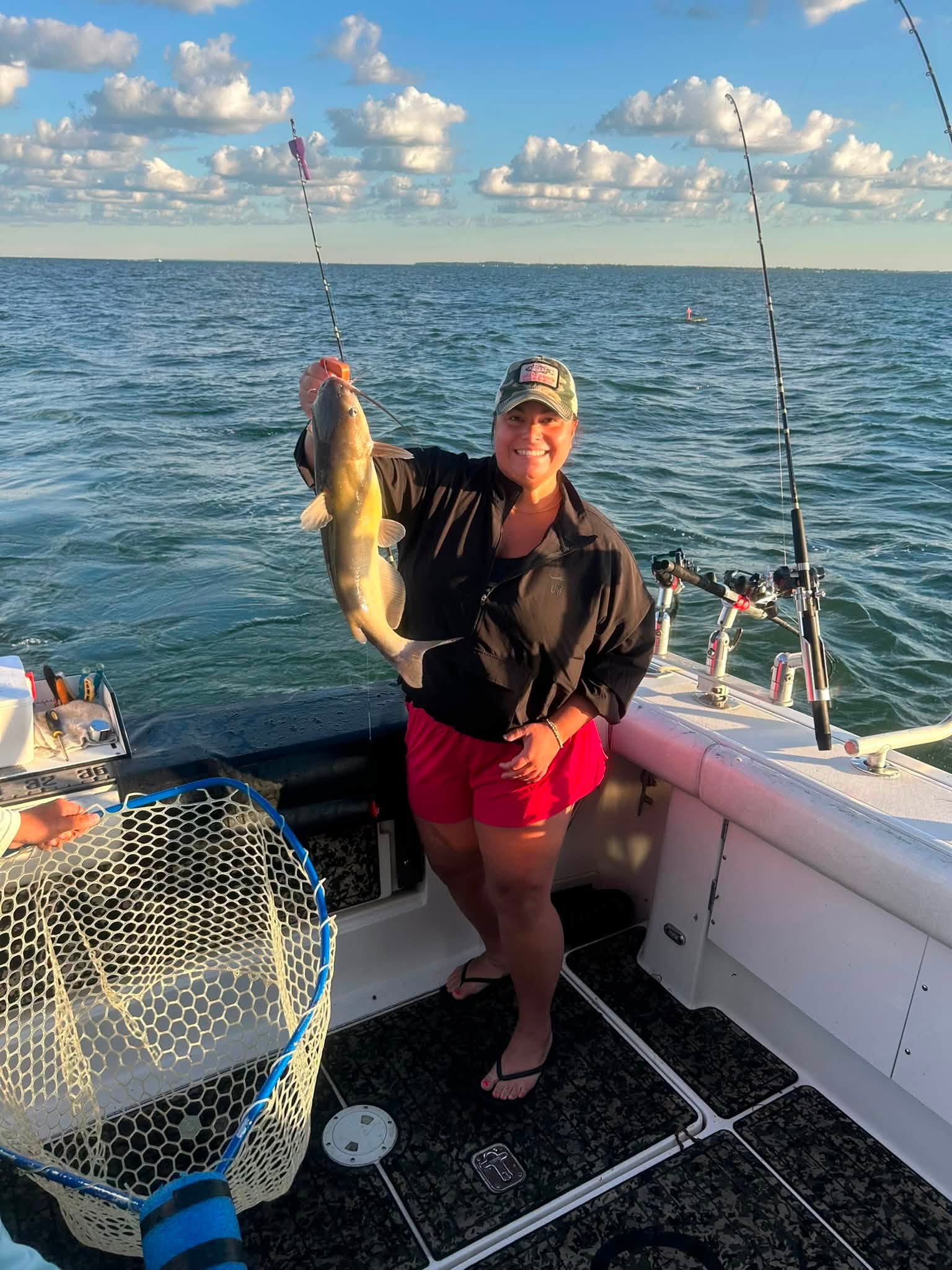 Angler holding freshly caught channel catfish on fishing boat with net and rods visible