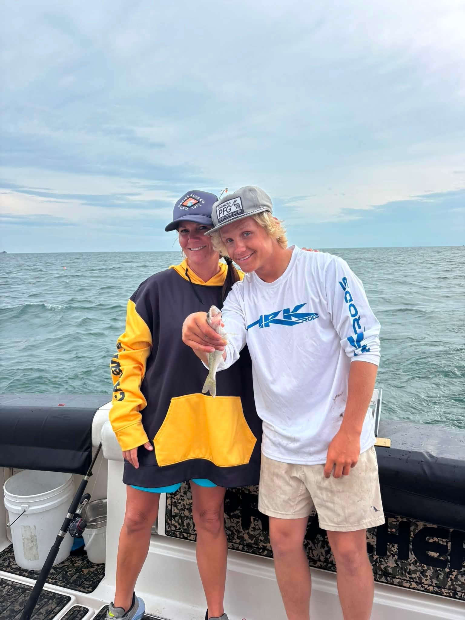 Two anglers on fishing boat holding freshly caught fish on the water