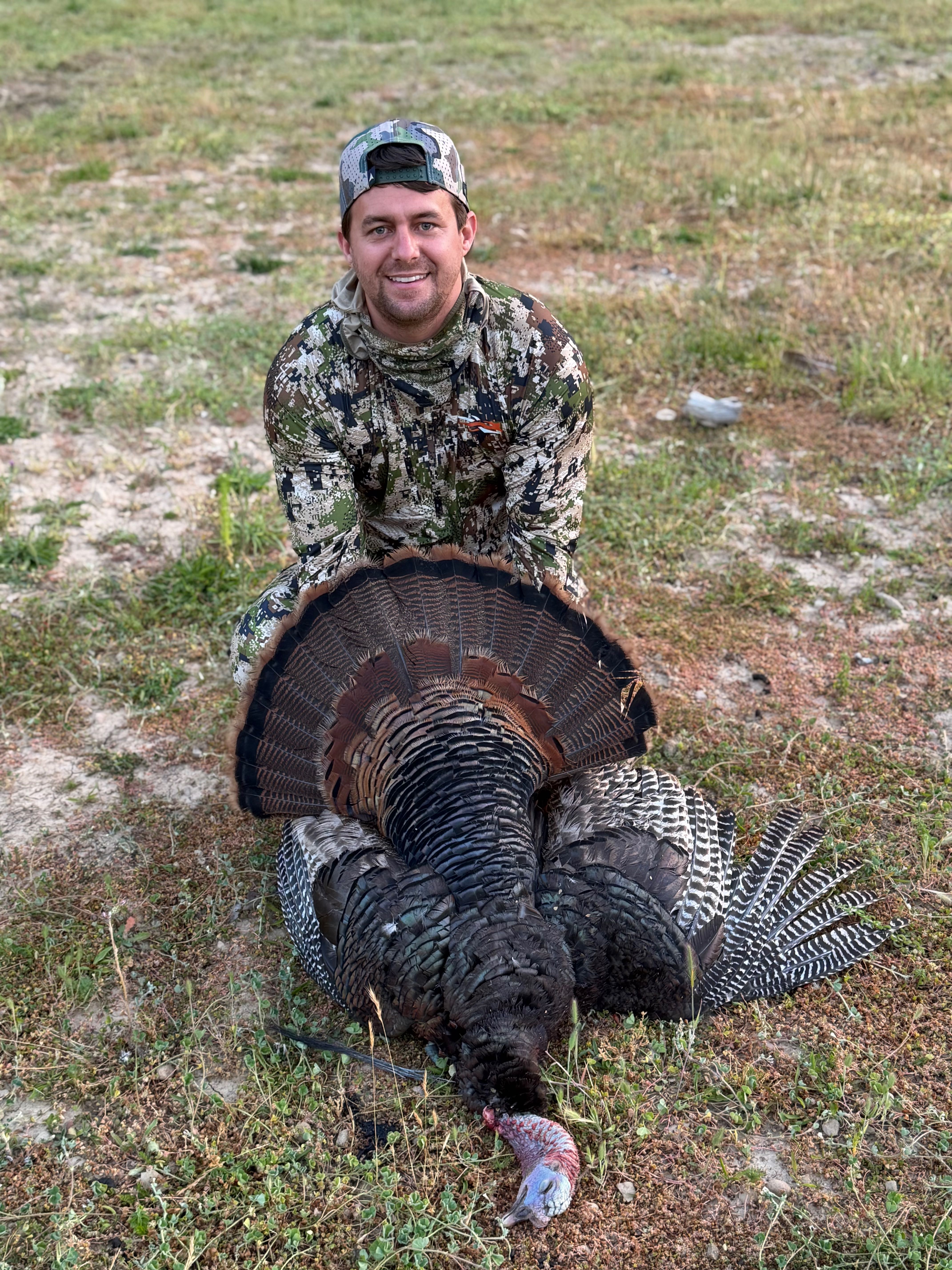 Hunter posing with harvested turkey displaying tail fan in Winchester Bay Oregon field