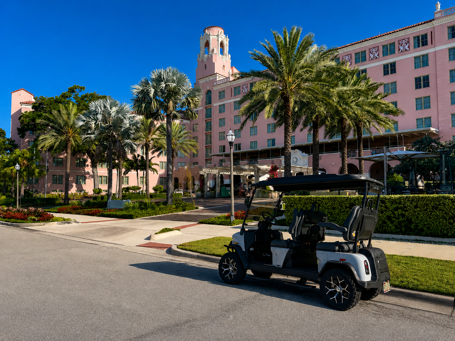 Golf cart parked on street in front of pink resort hotel with palm trees and bell tower