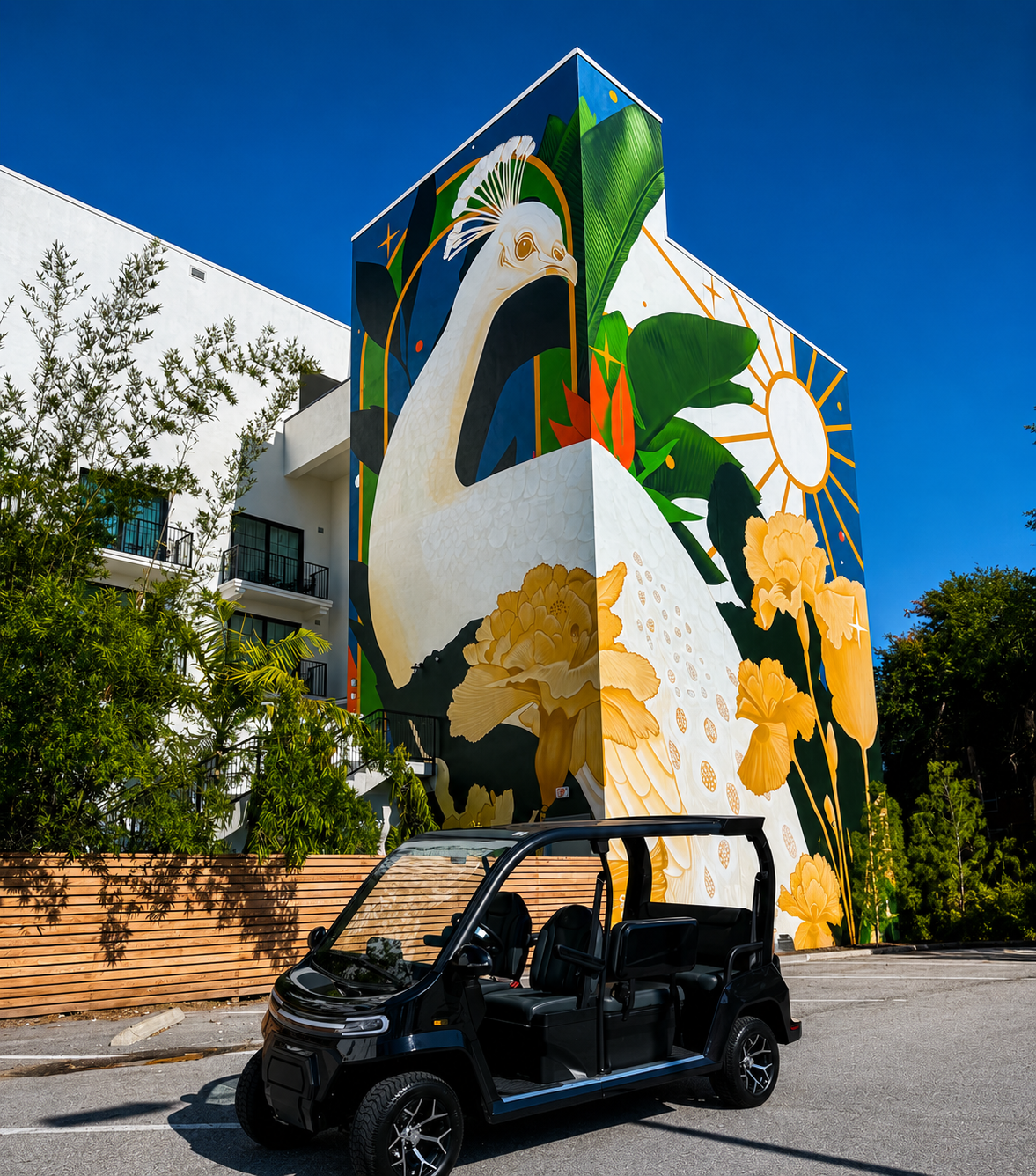 Colorful mural featuring white bird with tropical flowers on building wall next to golf cart