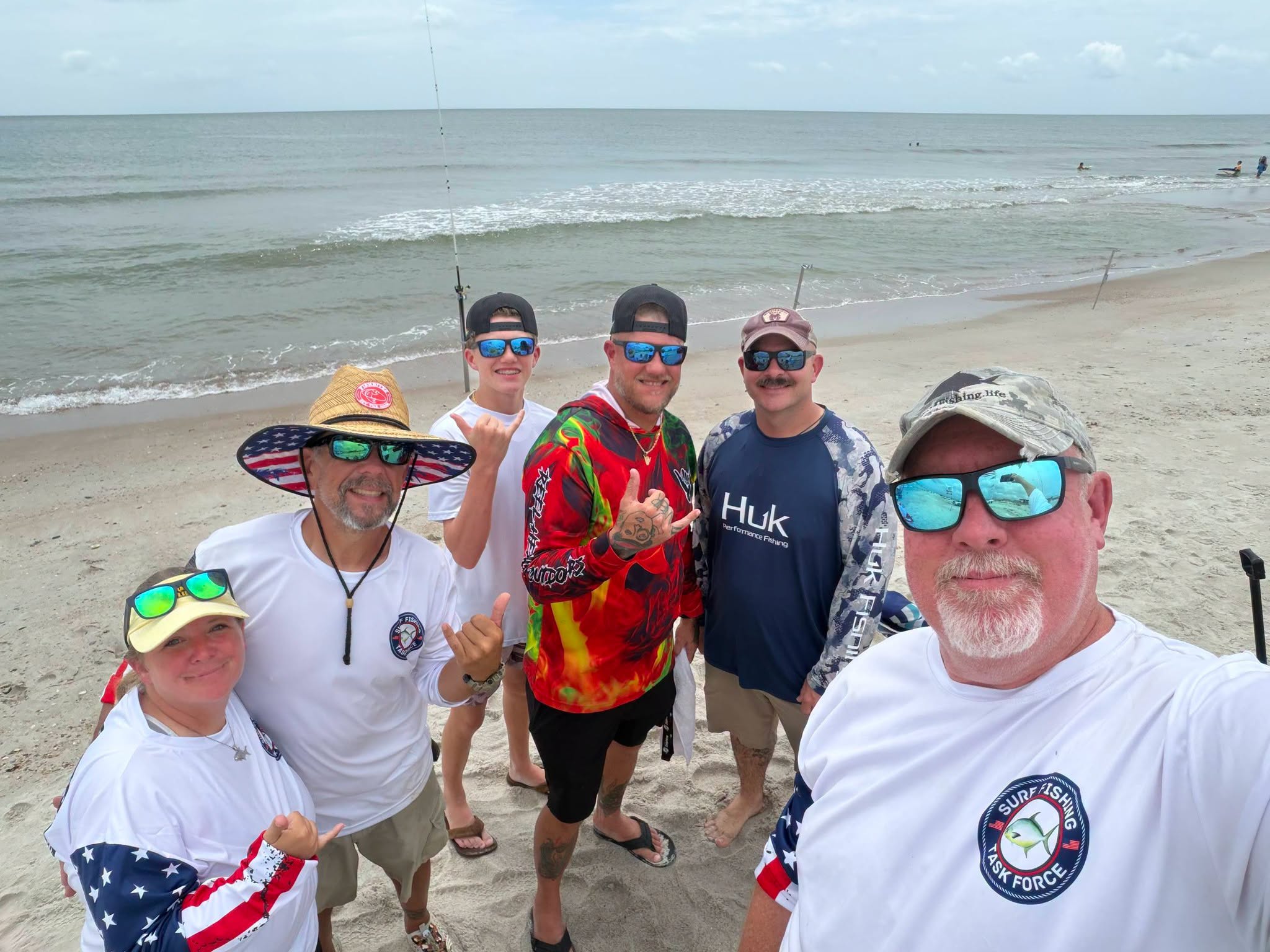 Group of anglers posing together on New Smyrna Beach FL with fishing rods and ocean waves in background