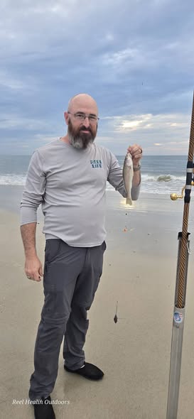 Angler holding caught fish on New Smyrna Beach FL shoreline with fishing rod visible