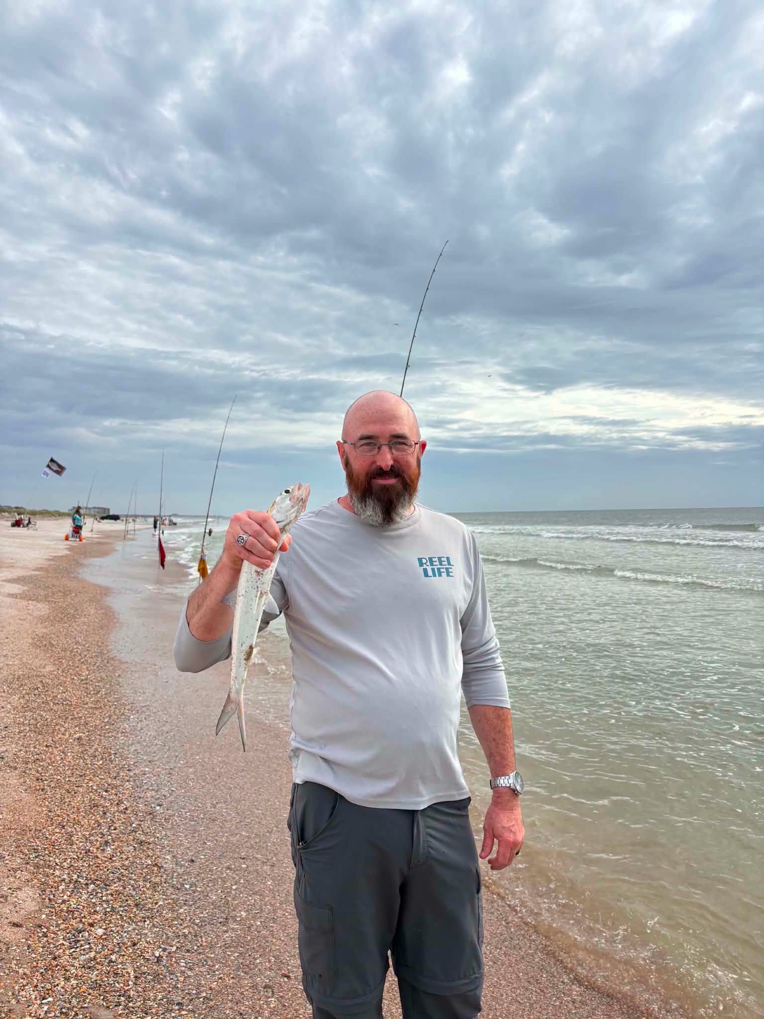 Angler holding caught fish on New Smyrna Beach FL shoreline with fishing rods in background