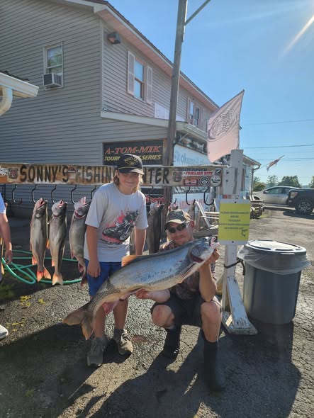 Large lake trout displayed at fishing charter dock in Pulaski NY with multiple fish hanging in background