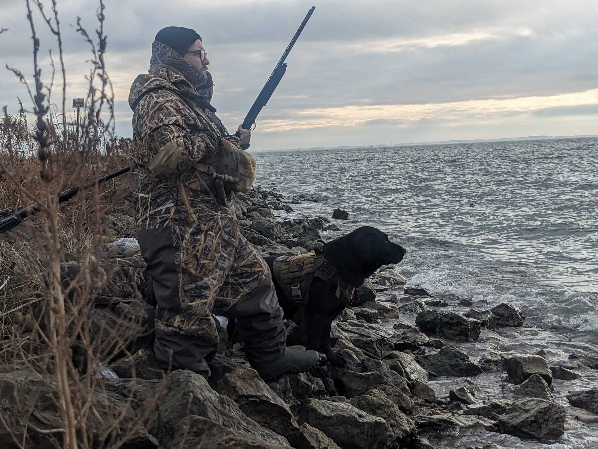 Hunter with black dog sitting on rocky shoreline near water in Detroit MI