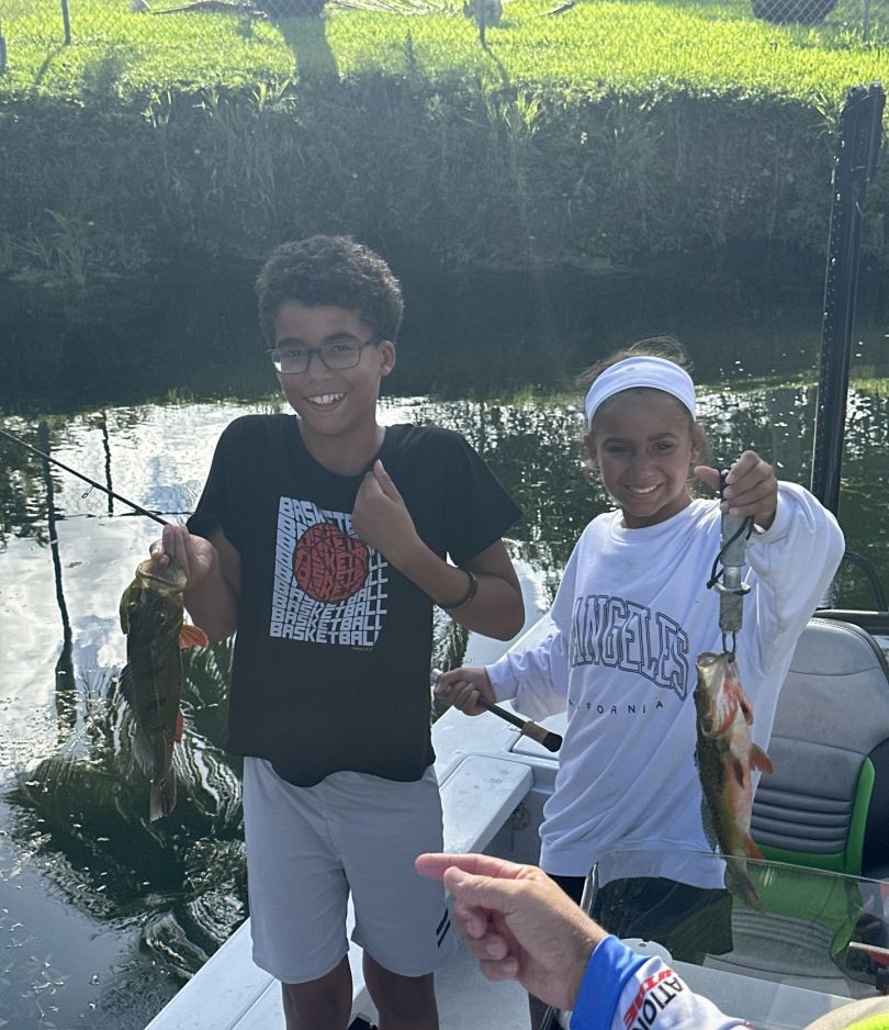 Two anglers displaying caught peacock bass and largemouth bass while fishing in Palmetto Bay FL