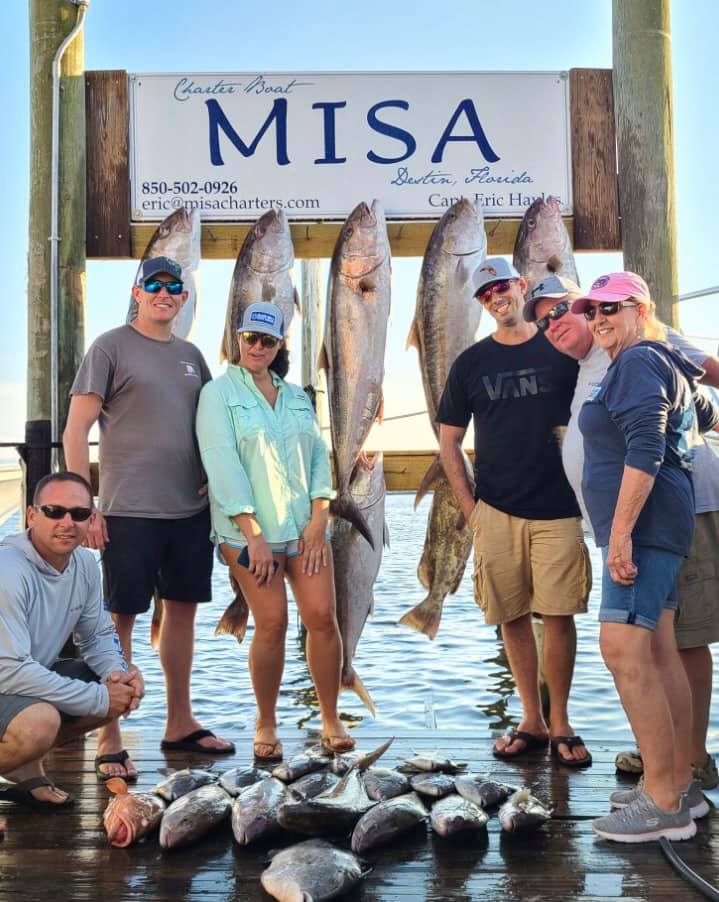 A group of 5 people enjoying a fishing trip in Destin, holding 3 big fish