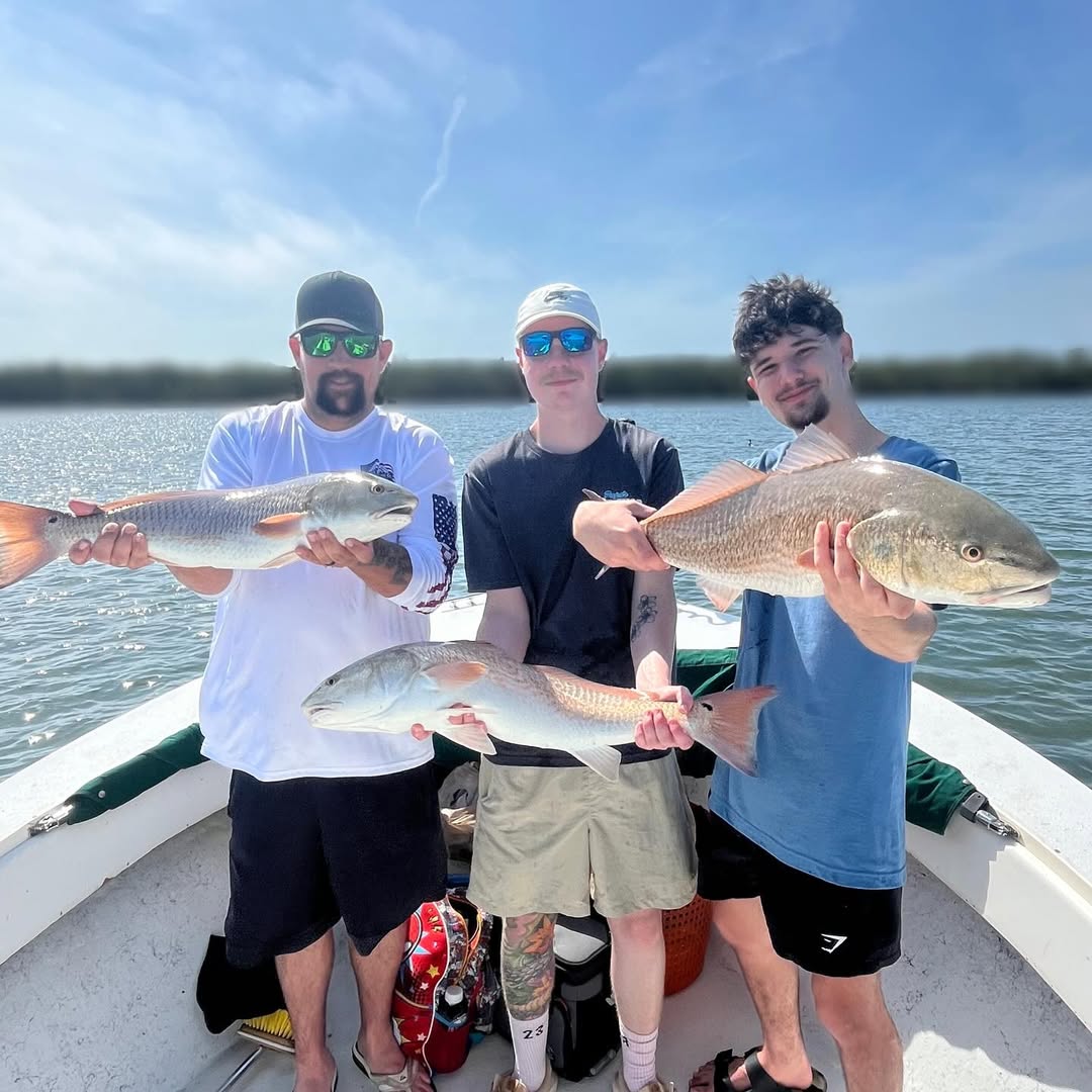 Three anglers displaying caught redfish on fishing boat in Holmes Beach FL