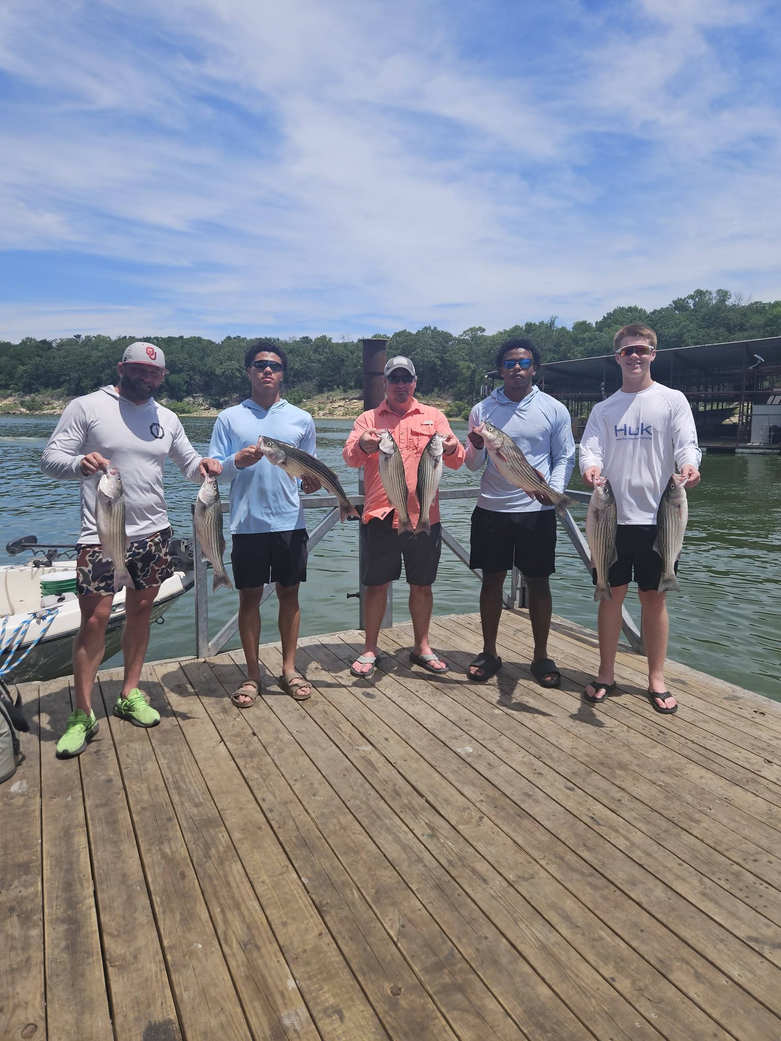 Five anglers displaying their striped bass catch on wooden dock at Kingston OK