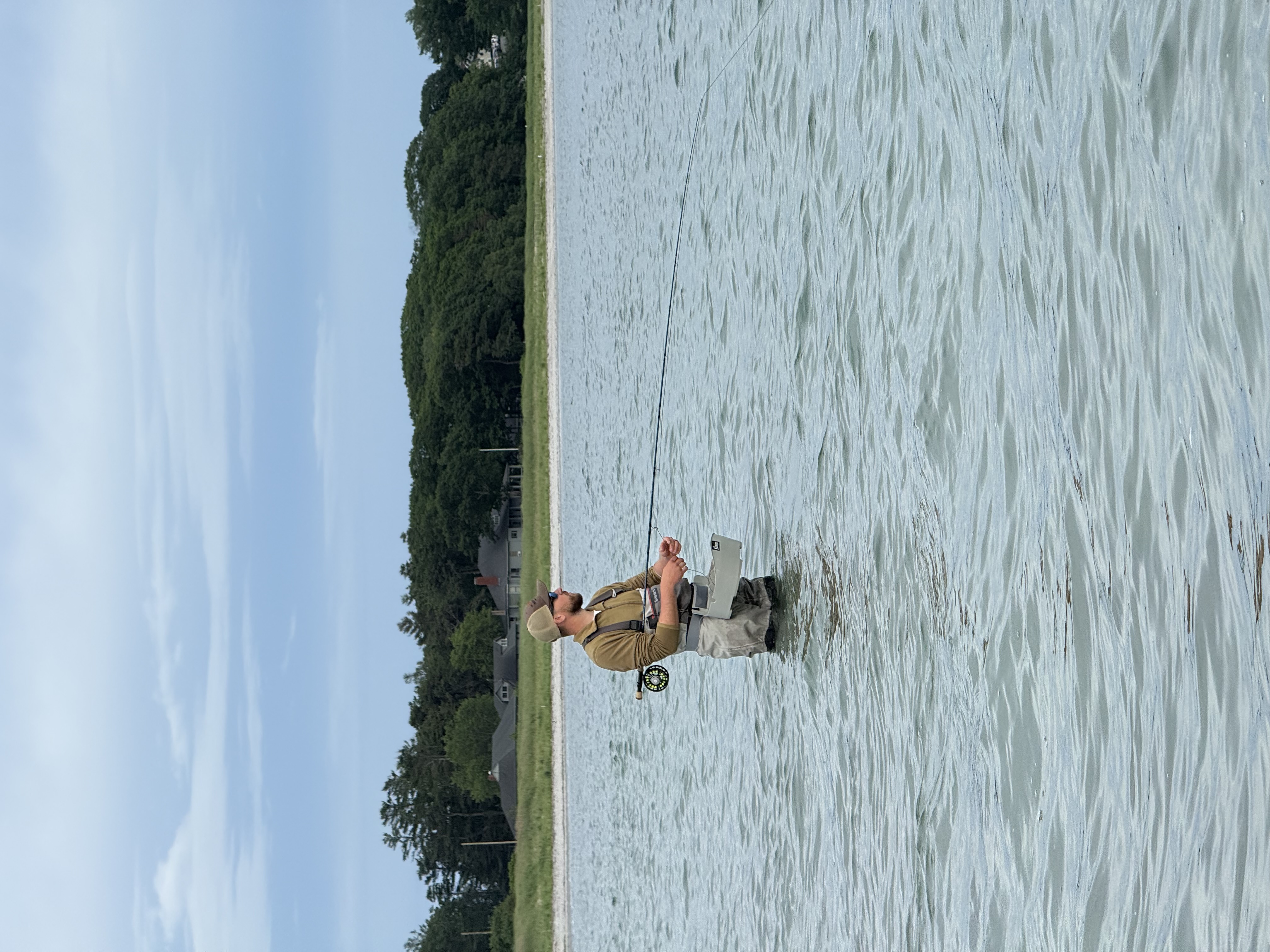 Fishing guide wading in calm water near wooded shoreline in South Portland Maine