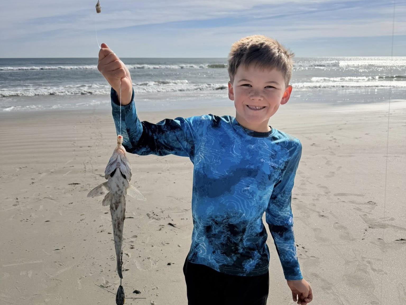 Surf fishing guide with rod on Fernandina Beach sand casting into Atlantic Ocean waves