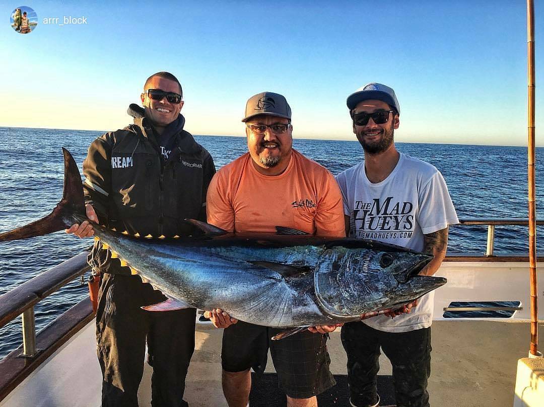 Three anglers displaying large bluefin tuna catch on fishing boat deck in Collinsville TX