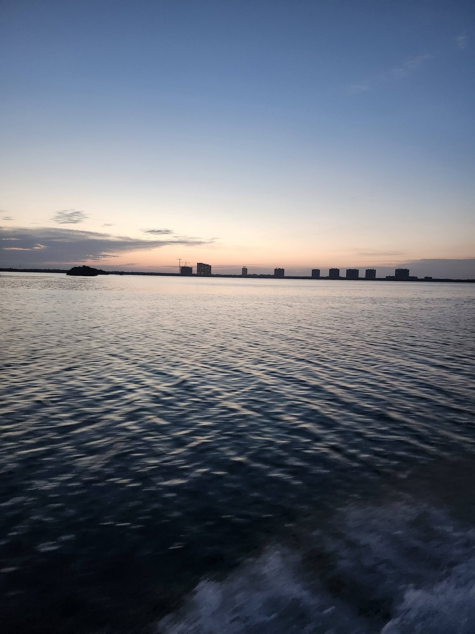 Fishing boat wake on calm water at sunset with Bonita Springs FL skyline in distance