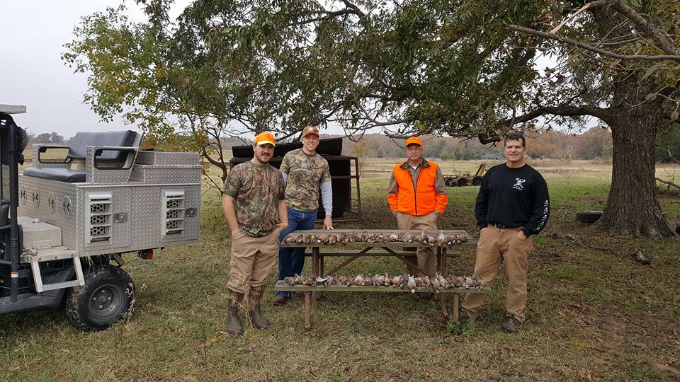 Hunting party displaying harvested game birds on table under tree in Alba TX