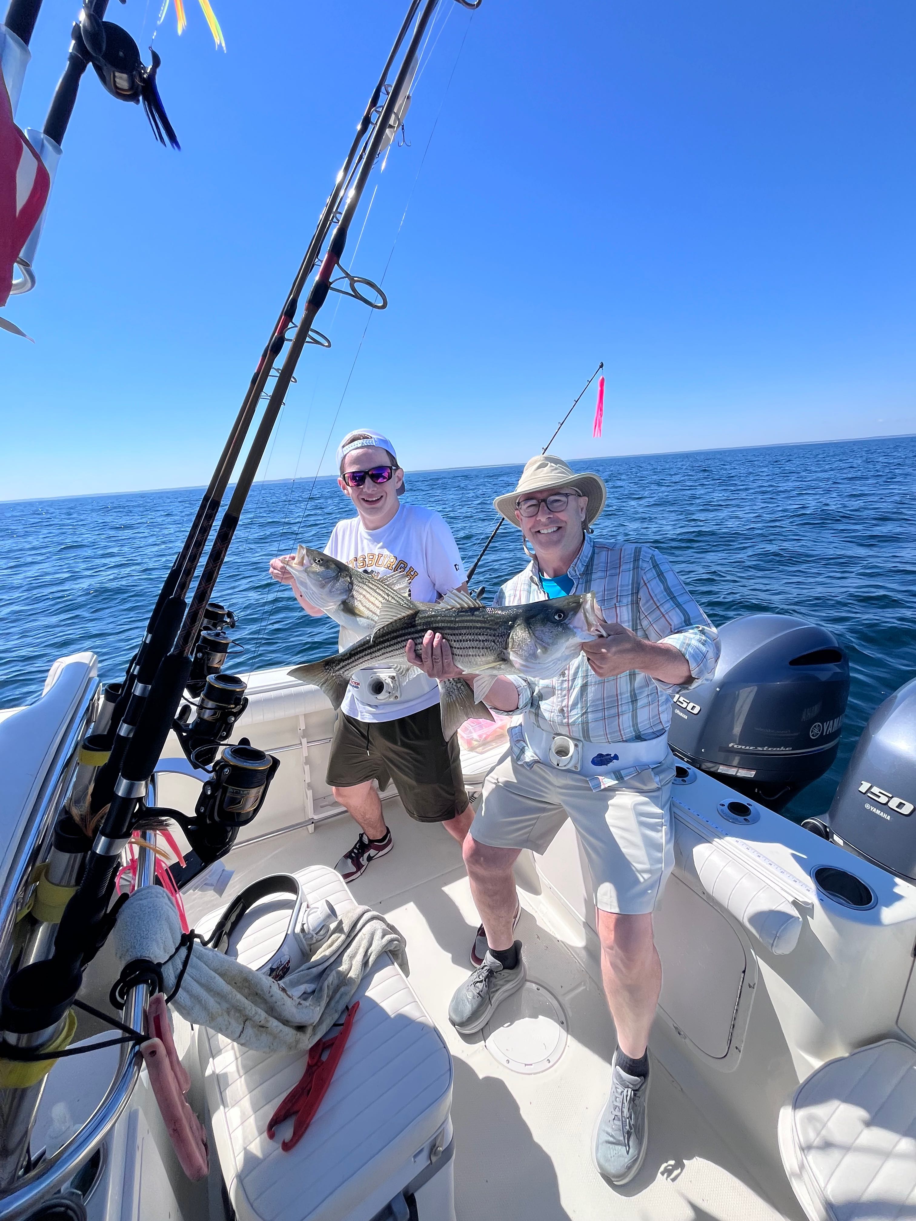 Two anglers holding striped bass on fishing boat in East Dennis MA waters