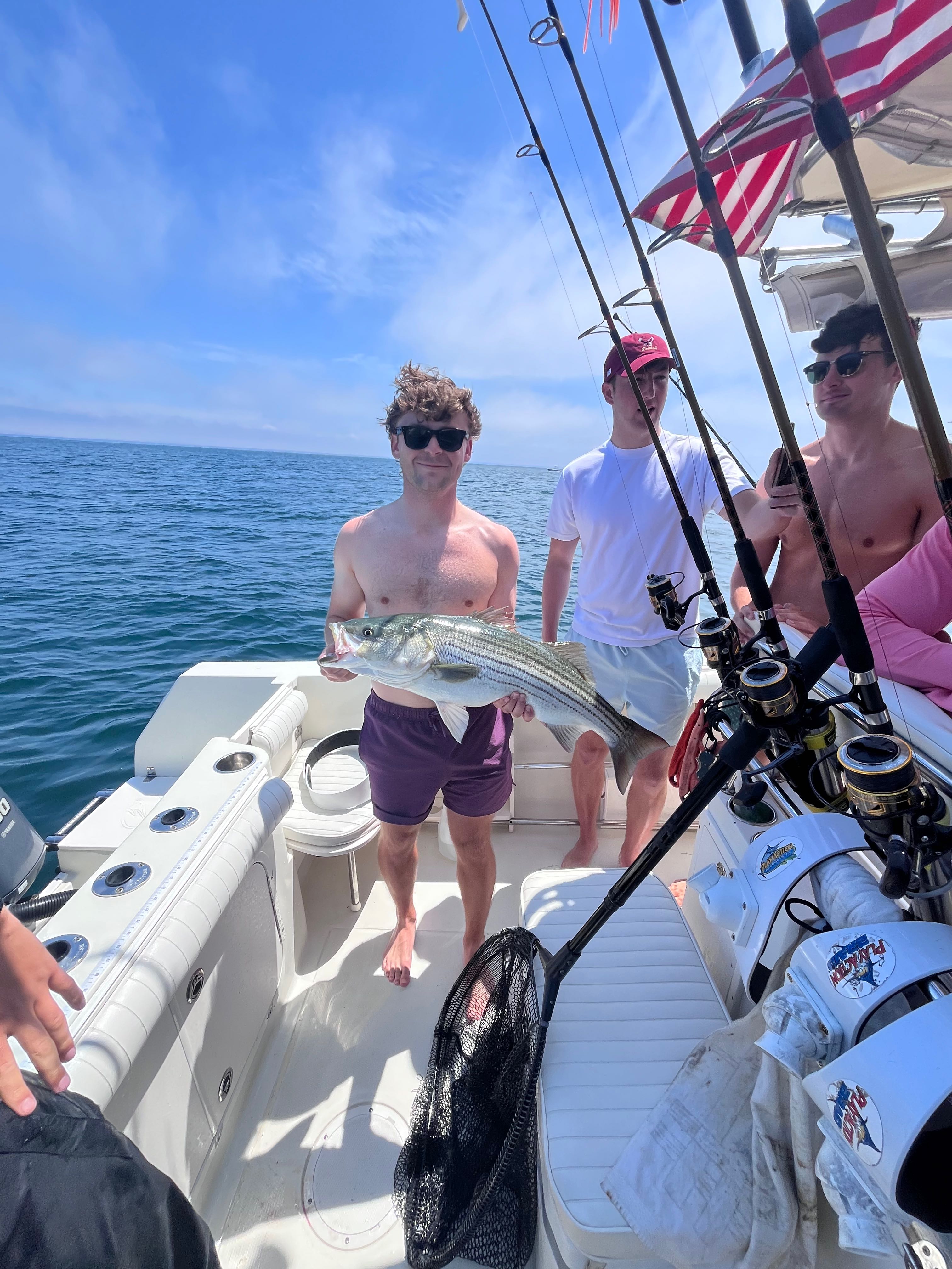 Striped bass caught during fishing charter in East Dennis MA with fishing boat and ocean backdrop