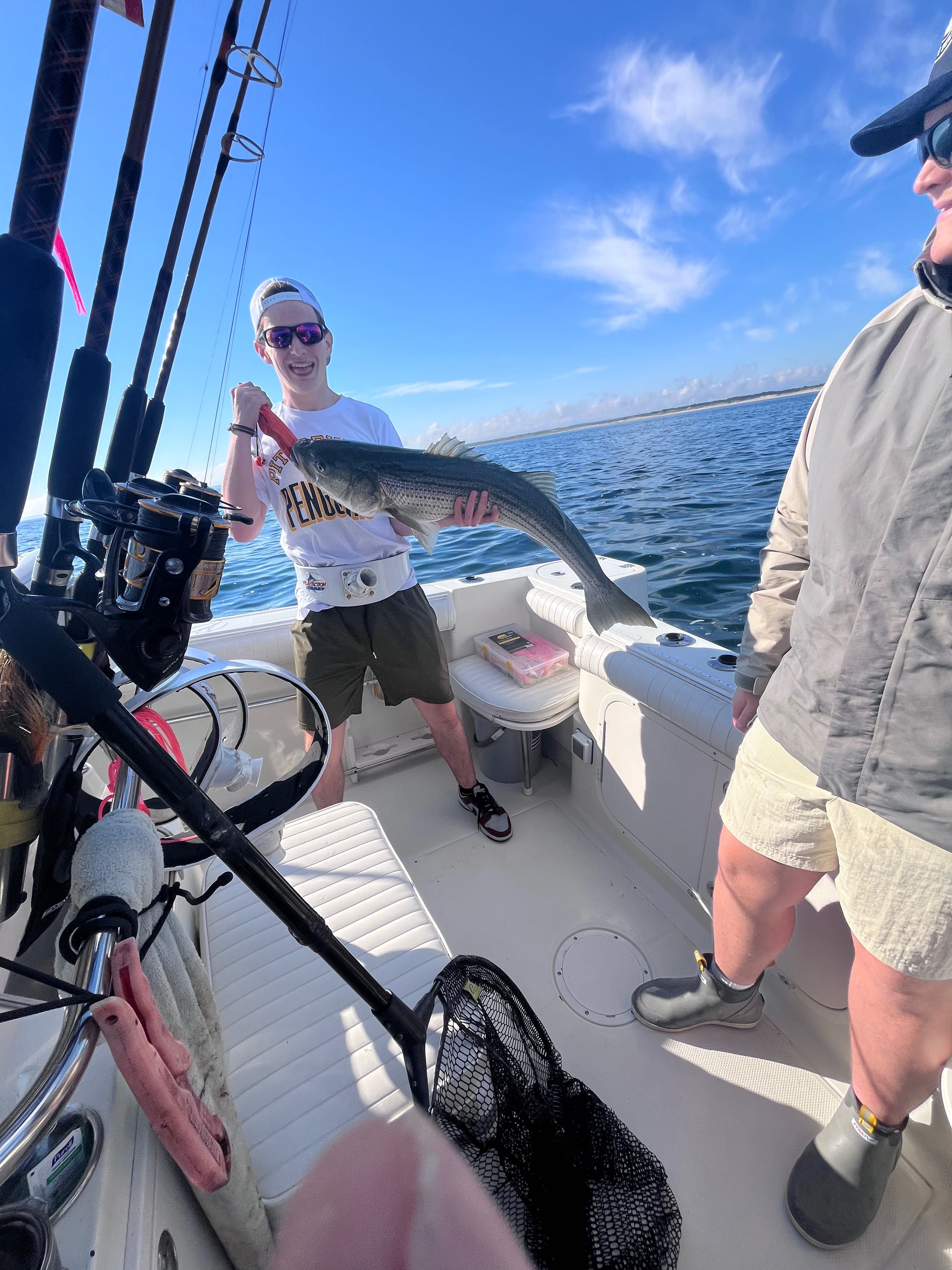 Striped bass caught during fishing charter in East Dennis MA with fishing rods and net visible on boat deck