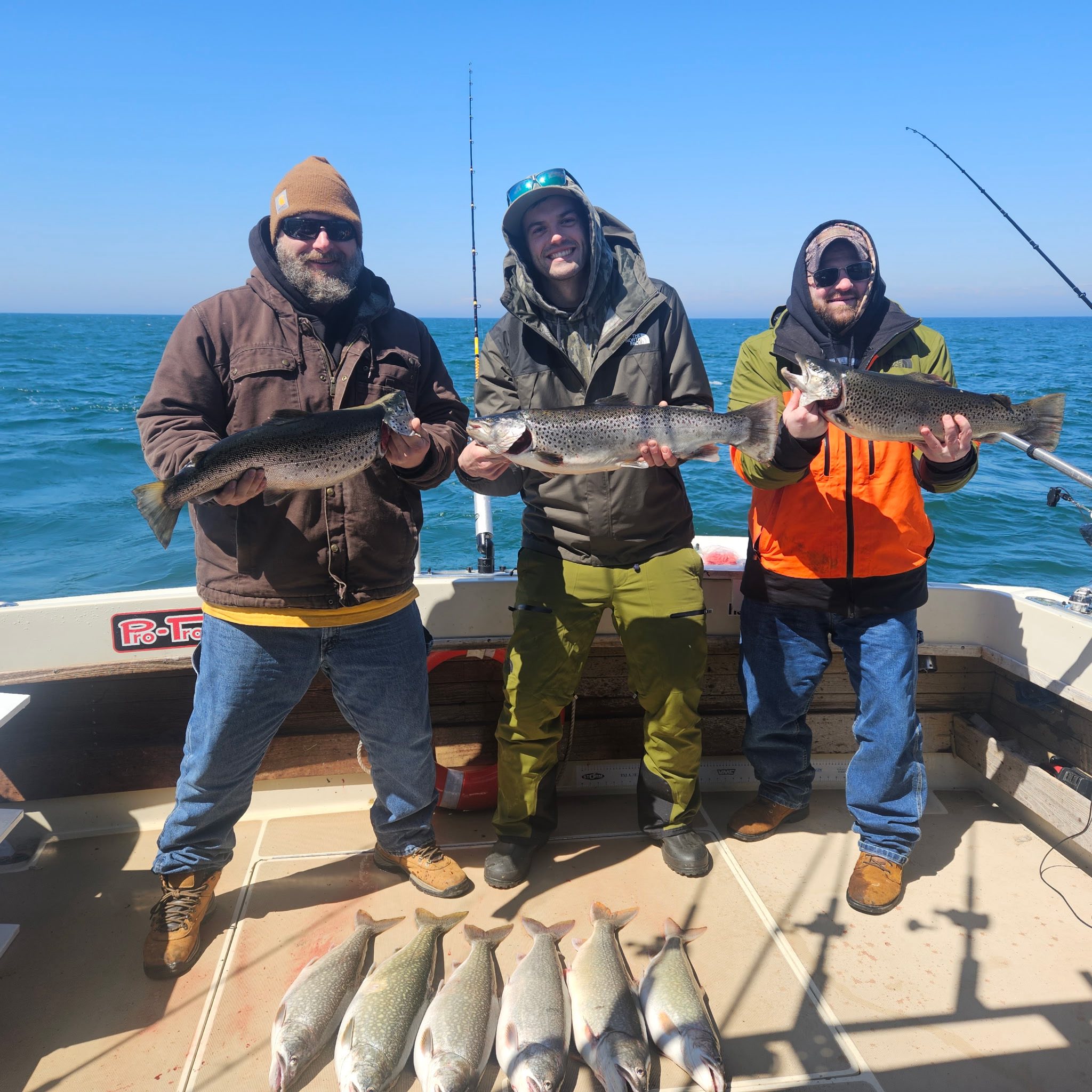 Three anglers displaying Atlantic salmon, brown trout, and lake trout catch on fishing boat in Mexico NY