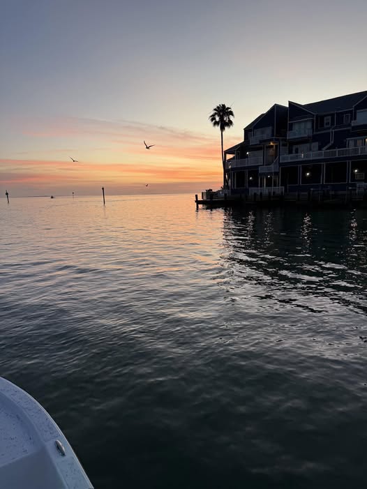 Sunset view from boat on calm water near waterfront buildings in South Padre Island TX during fishing trip